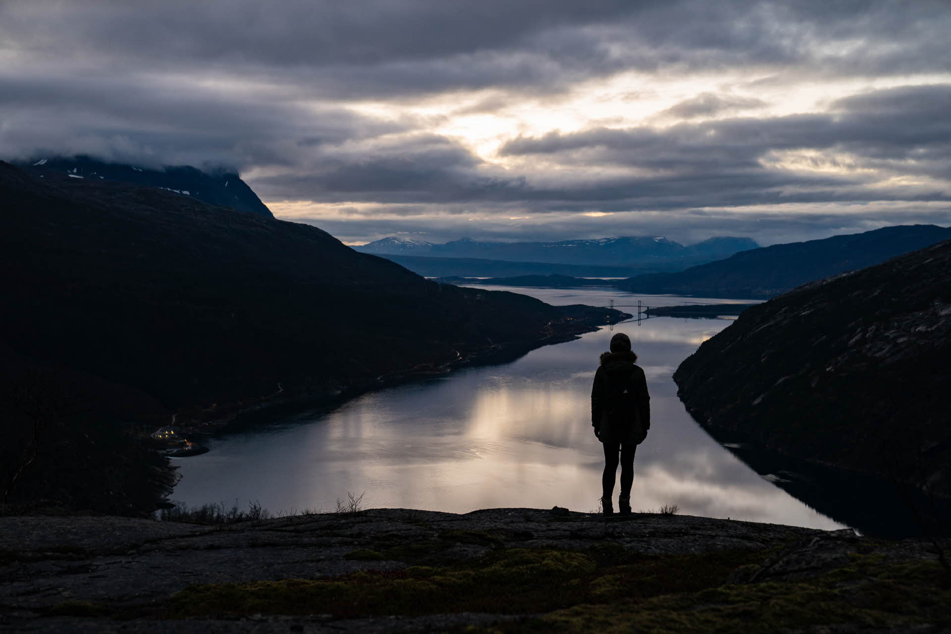 Silhouette einer Frau, die spätabends auf einem Berggipfel an der Ofoten-Linie steht und auf den Rombaksfjord blickt 