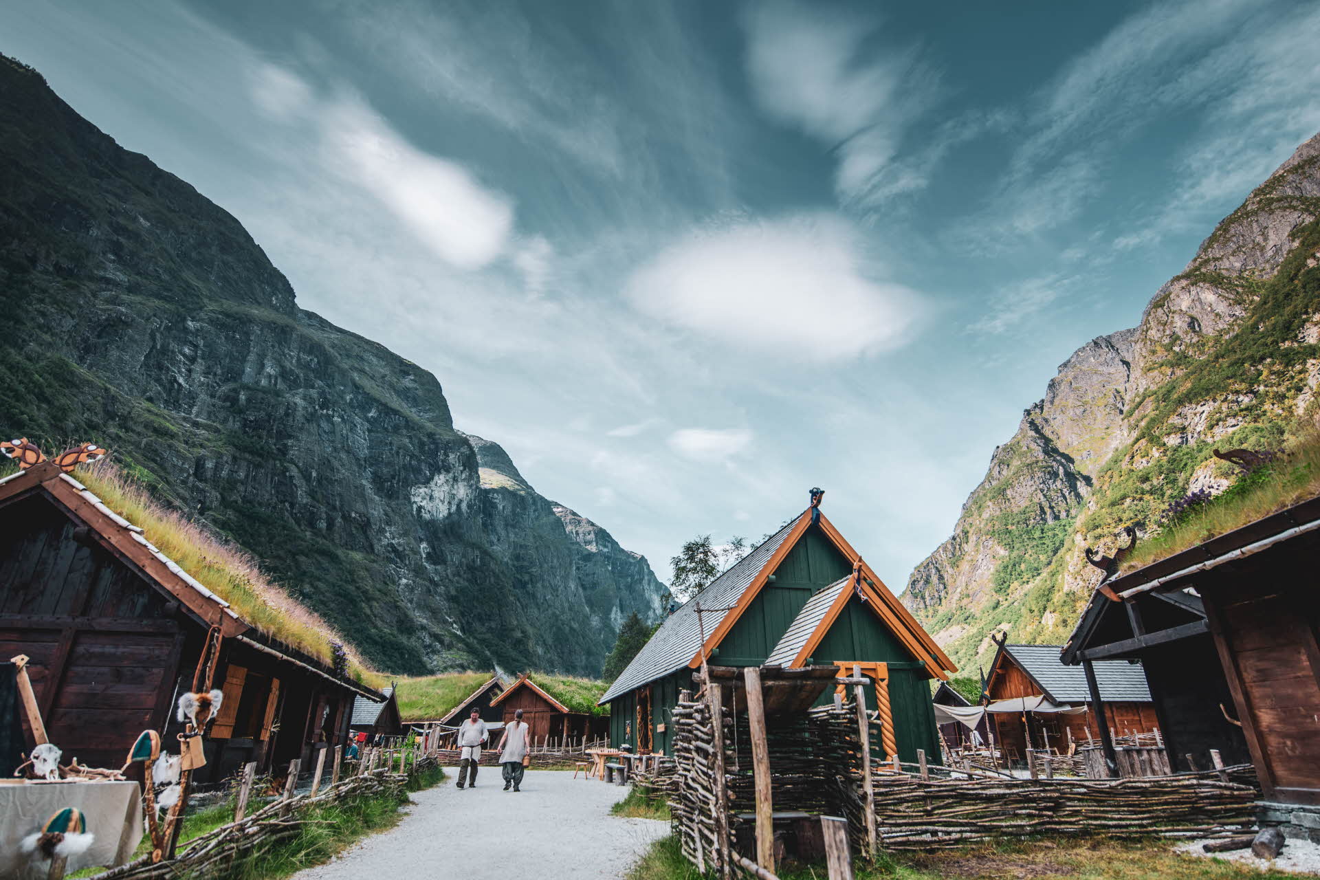 Bâtiments en bois brun, vert et jaune dans la Vallée viking. Deux hommes marchent sur un chemin.