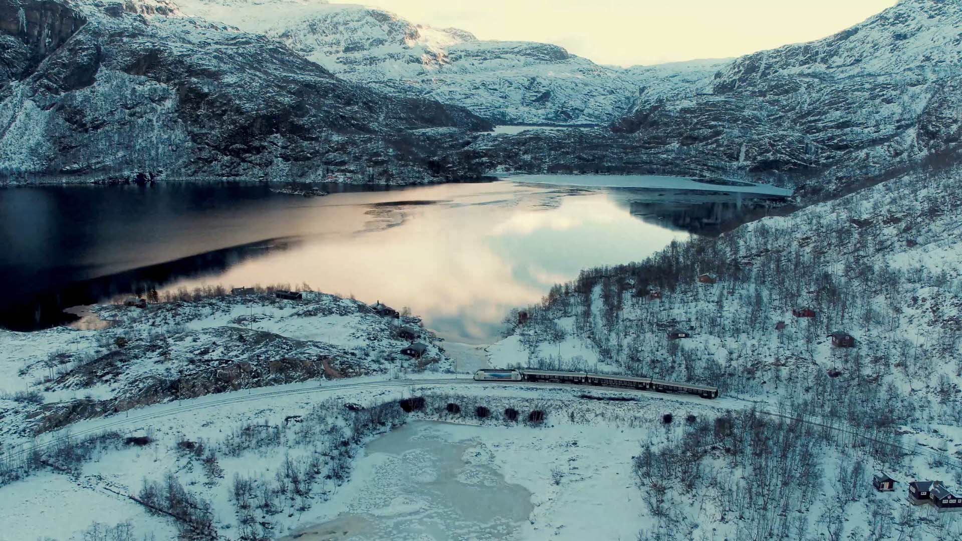 Die Flåmbahn durchquert die kalte Winterlandschaft an einem zugefrorenen See bei Sonnenuntergang
