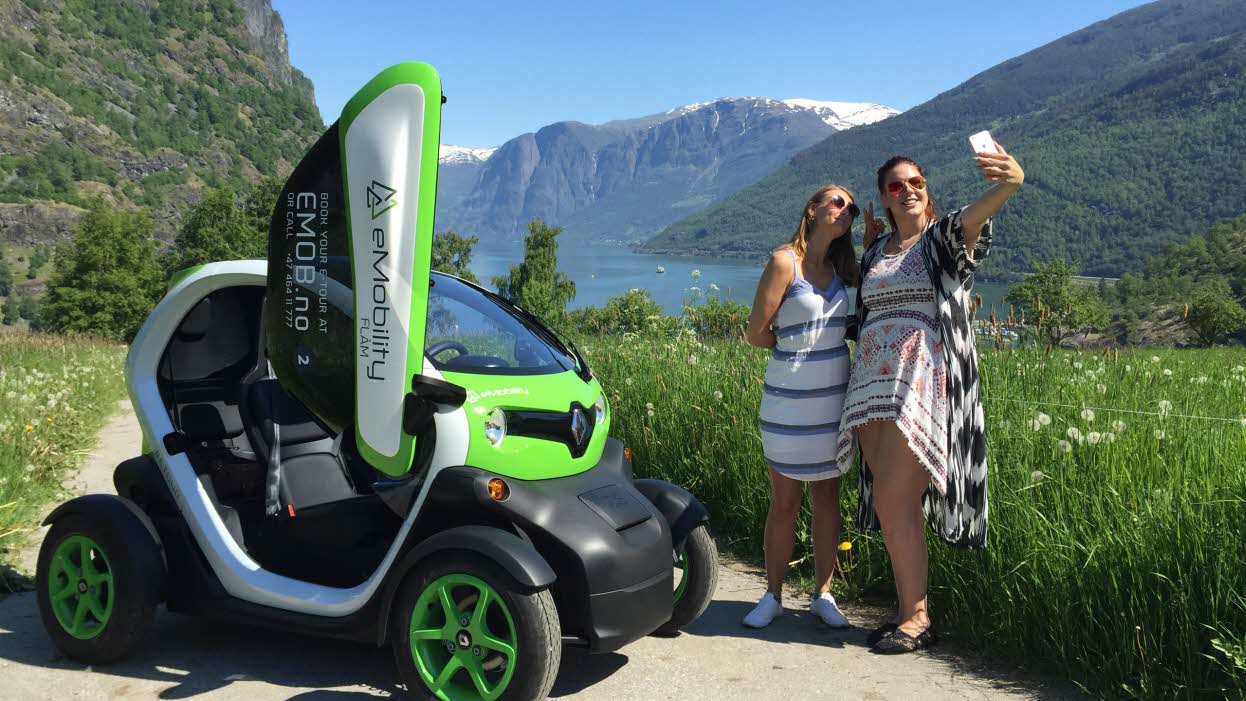 To kvinner tar selfie ved en liten elektrisk bil med Aurlandsfjorden i bakgrunnen