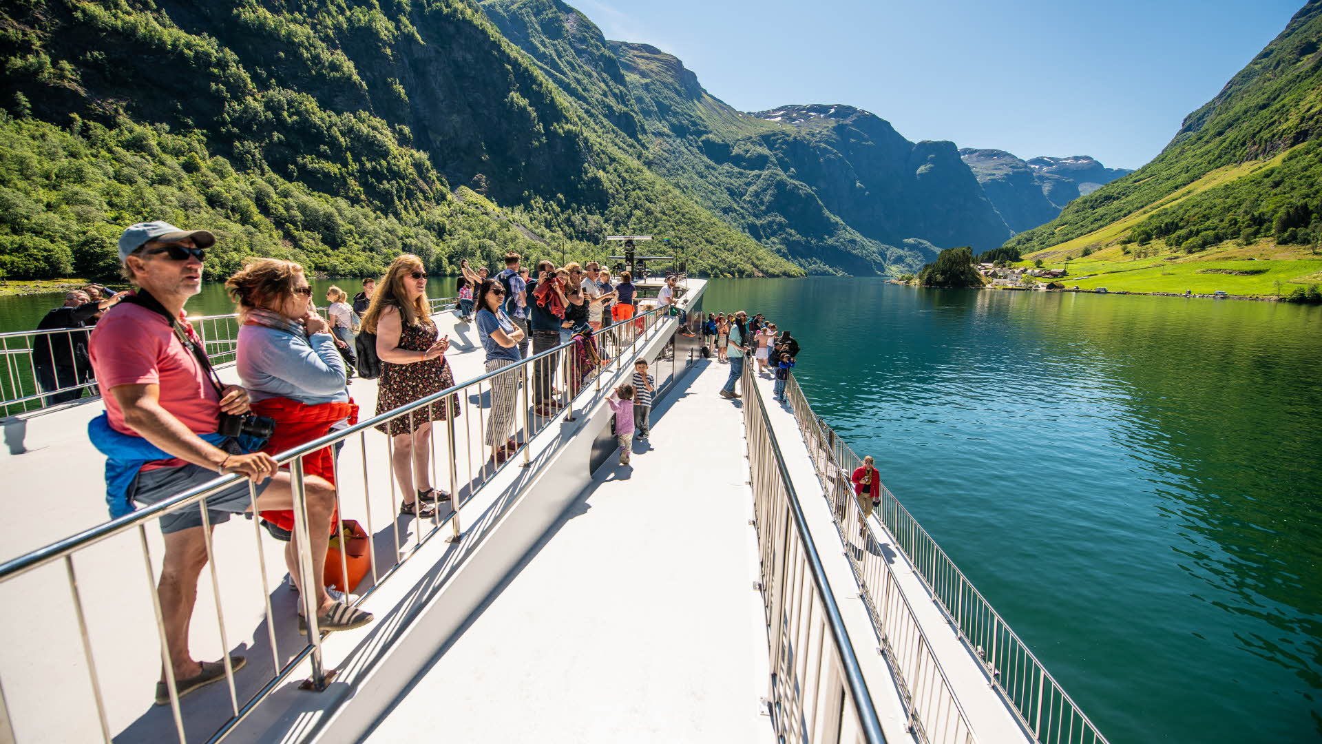 Folk som står utenfor ved svingede skinner om bord på Future of The Fjords i UNESCO-vernede Nærøyfjorden om sommeren