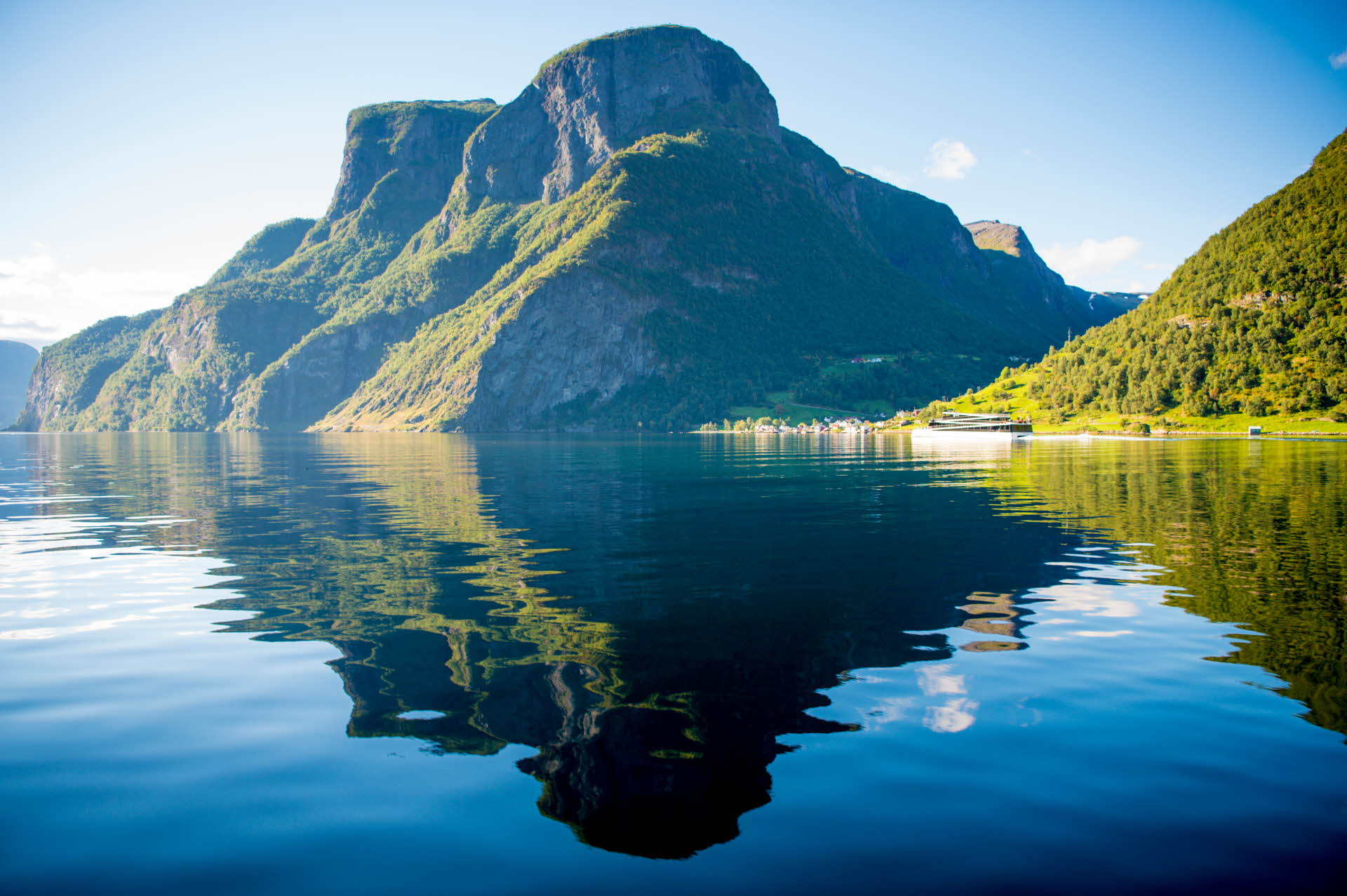 Steile Berge spiegeln sich an einem Sommertag im Nærøyfjord, in der Ferne ist die „Vision of The Fjords“ zu sehen