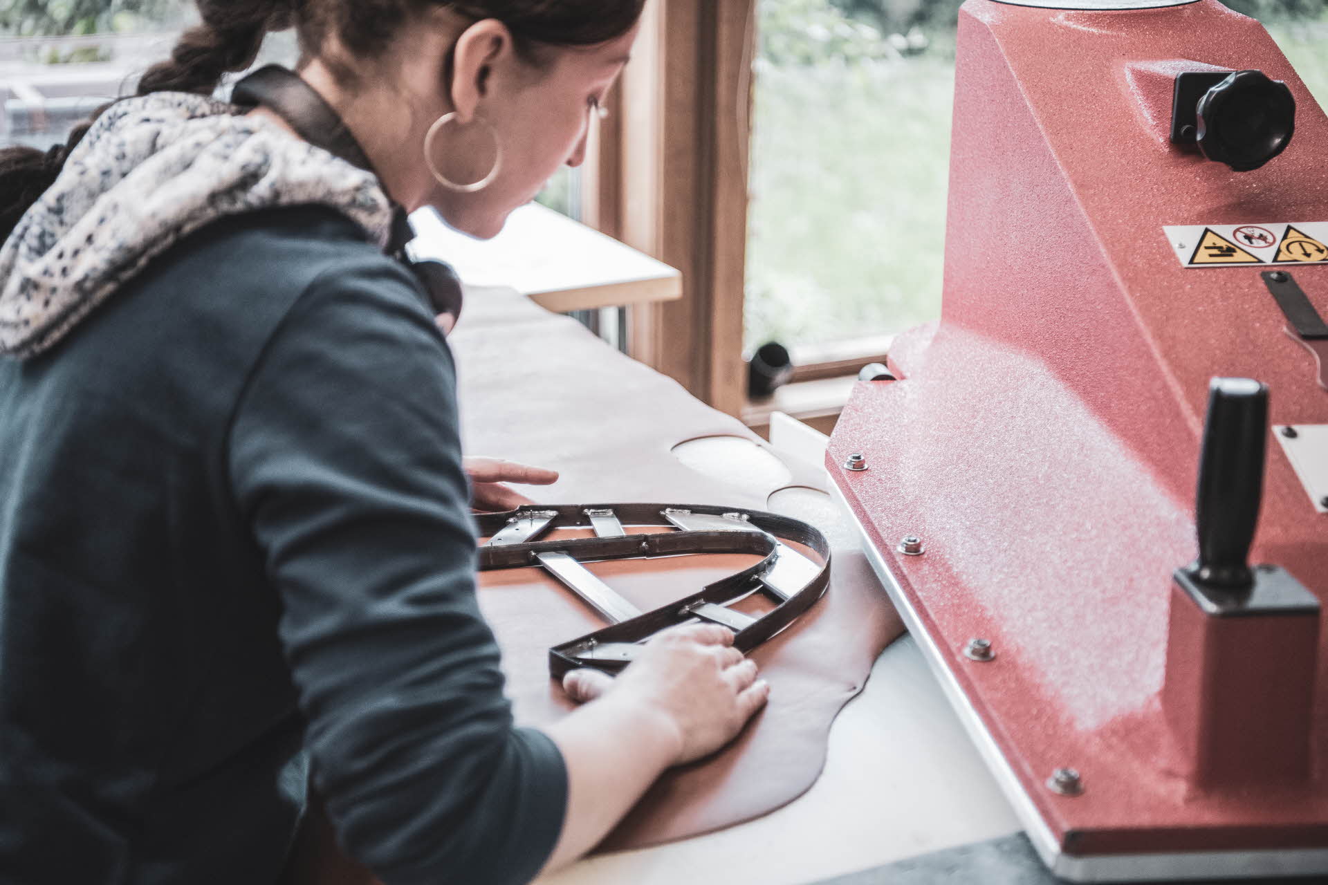 Une femme aligne avec précision un gabarit en acier tranchant pour découper des pièces de cuir de chaussures d’Aurland. La machine industrielle rouge est prête à la découpe. 