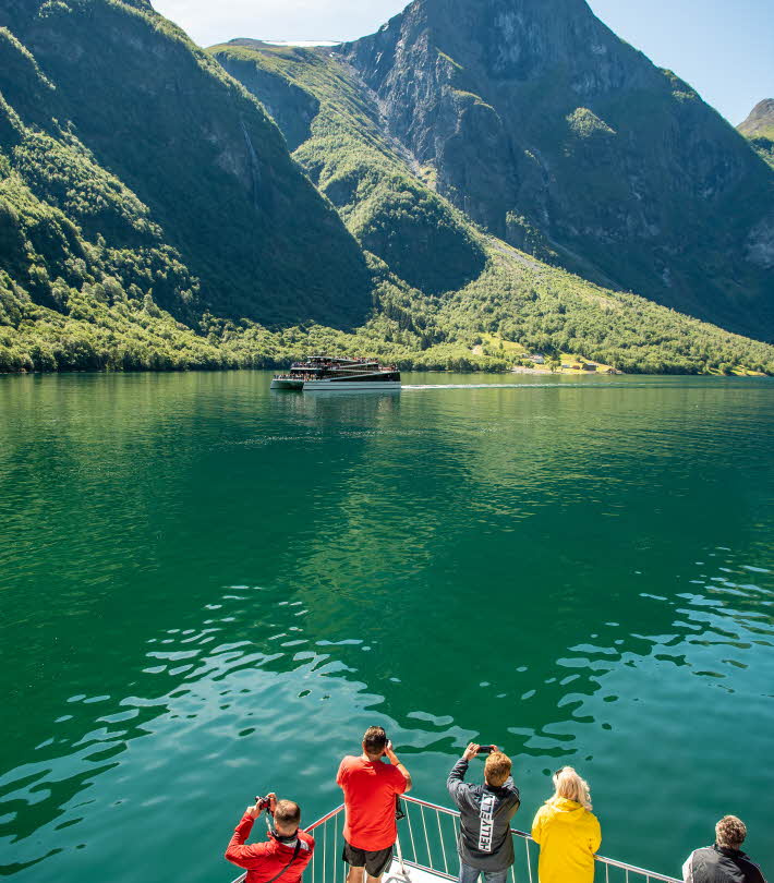 People standing on deck on board Fjord Cruise Nærøyfjord green sea and tall mountains summer day
