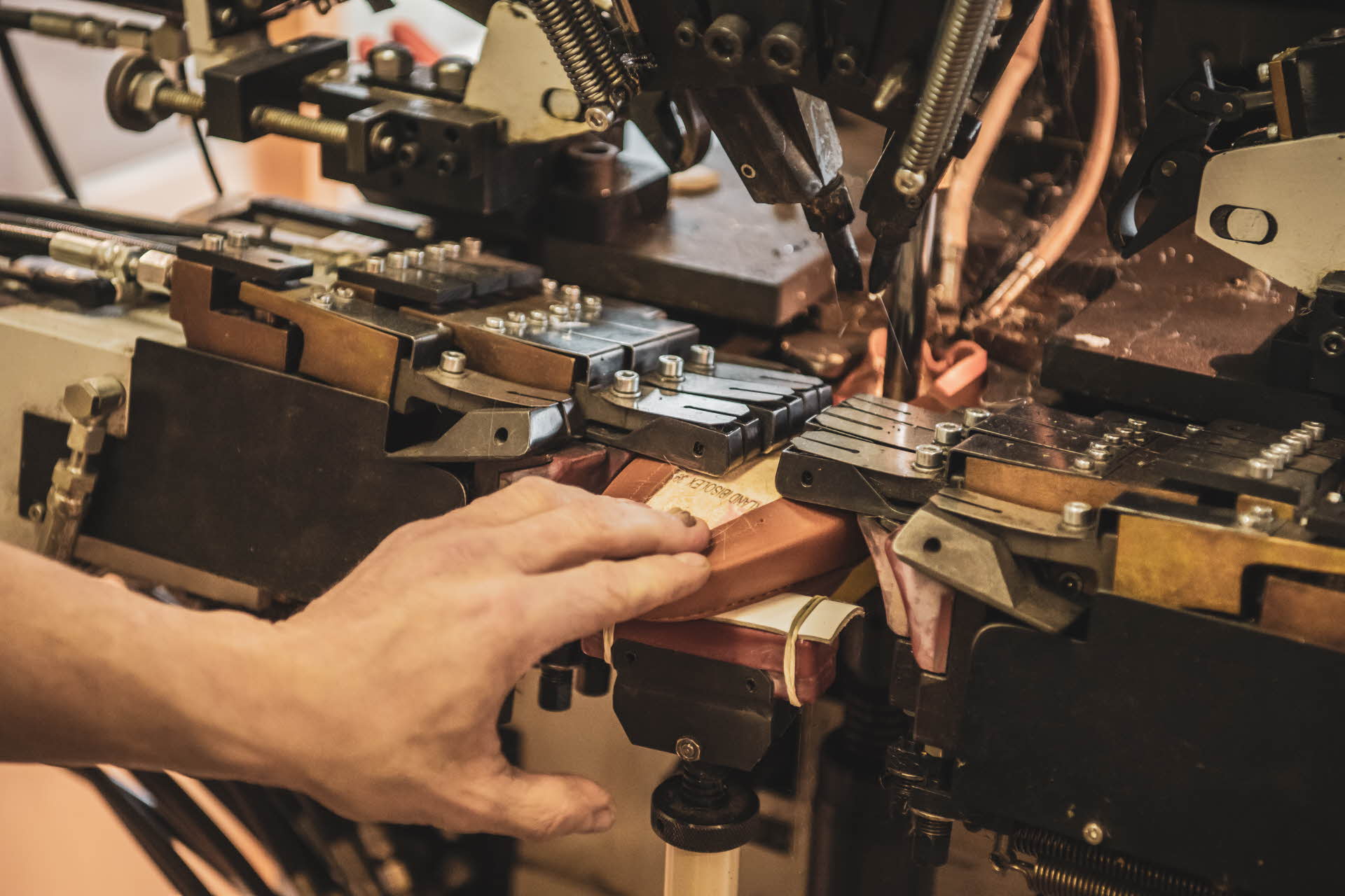工人们用手引导棕色奥兰鞋通过先进的机器，将皮革固定在内底。