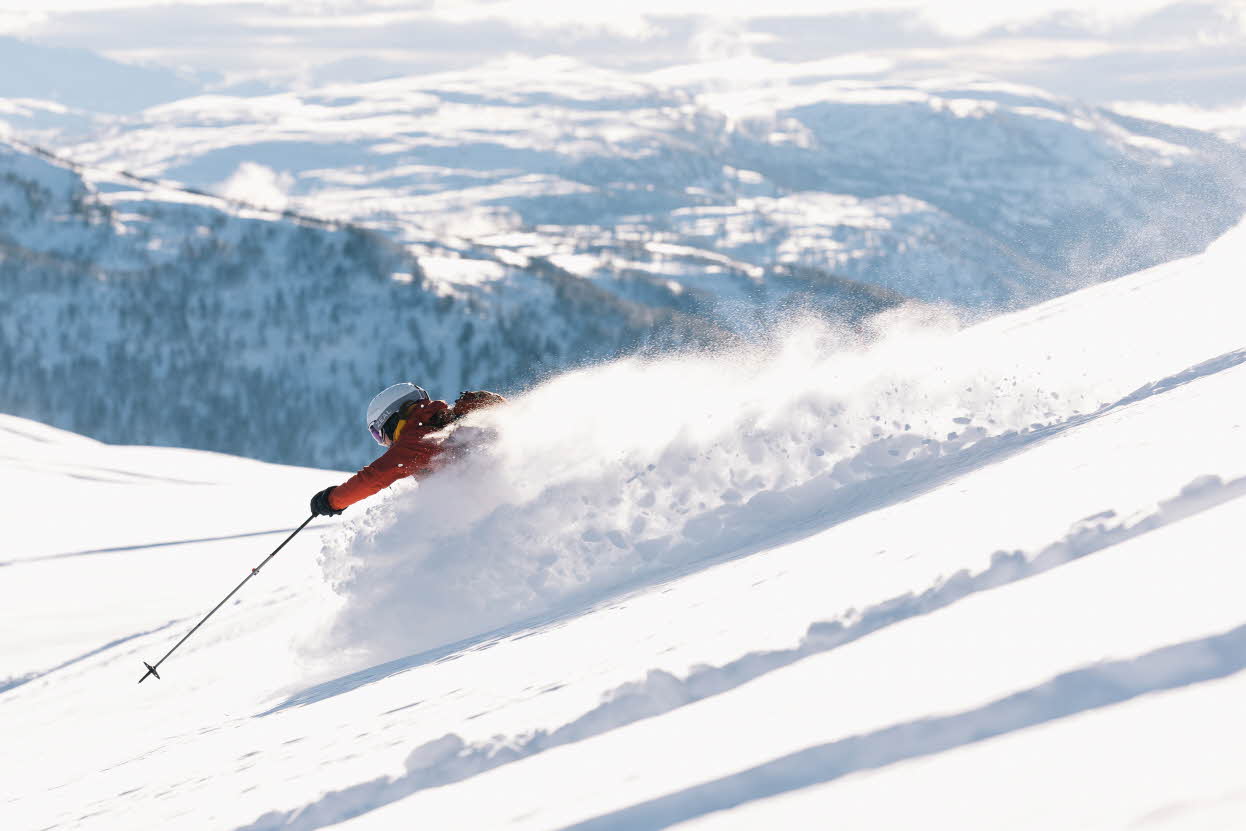 Ein Skifahrer wirbelt an einem sonnigen Tag in verschneiten Bergen Pulverschnee auf. Foto.