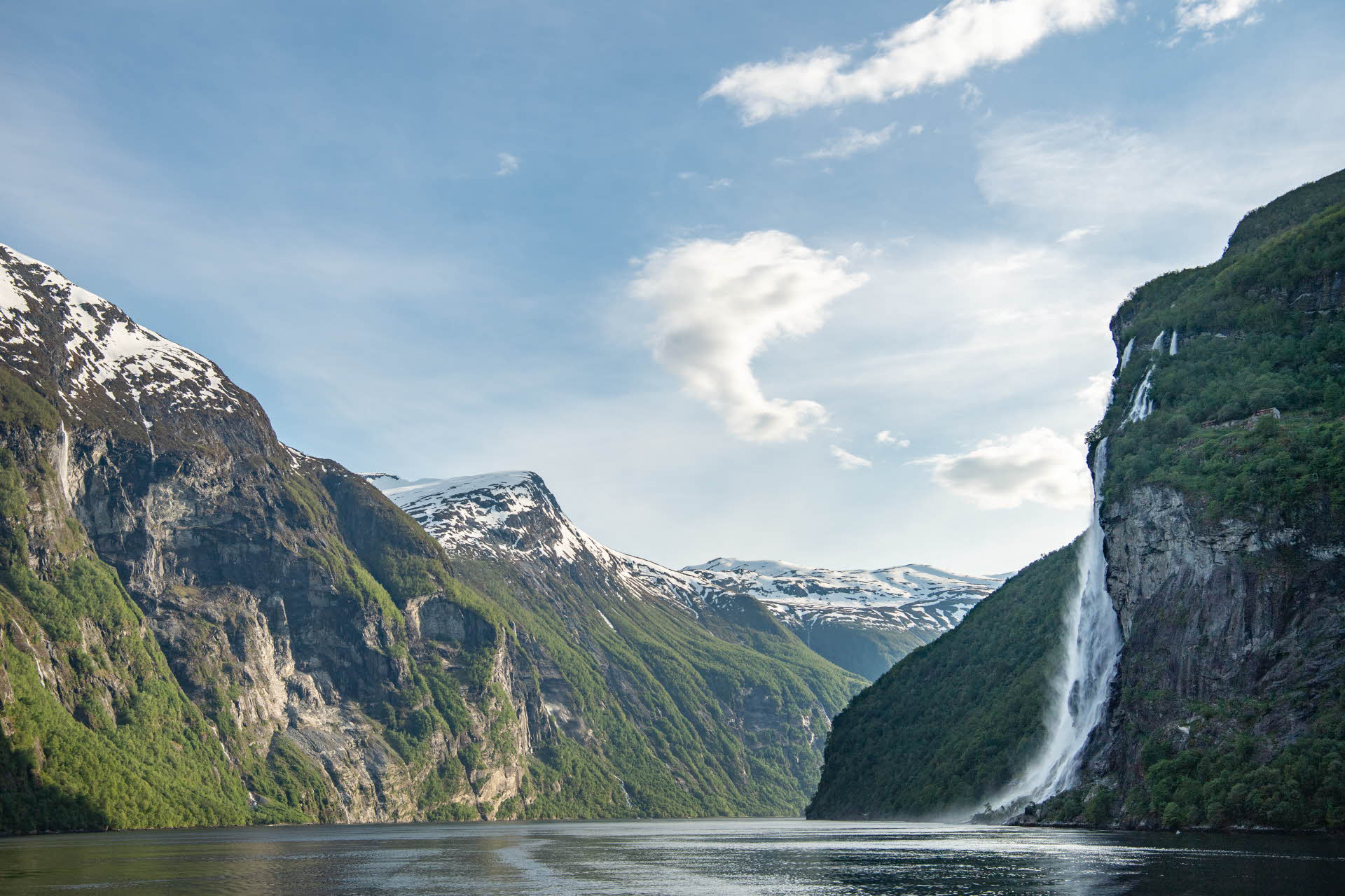 Der Geirangerfjord mit schneebedeckten Gipfeln und großem Wasserfall an einem Frühlingstag  