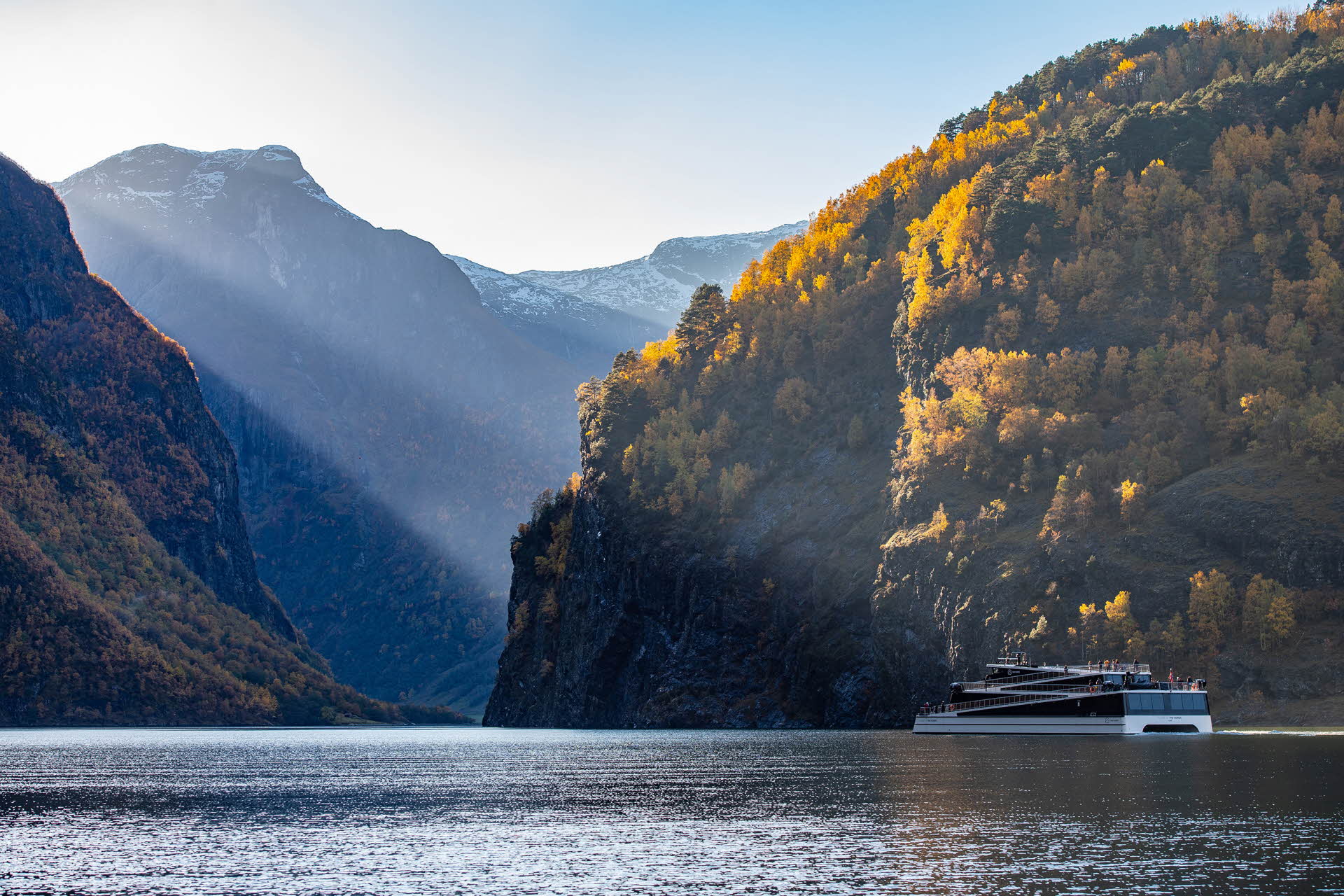 A modern vessel sailing into the Nærøyfjord. Yellow coloured mountains around.