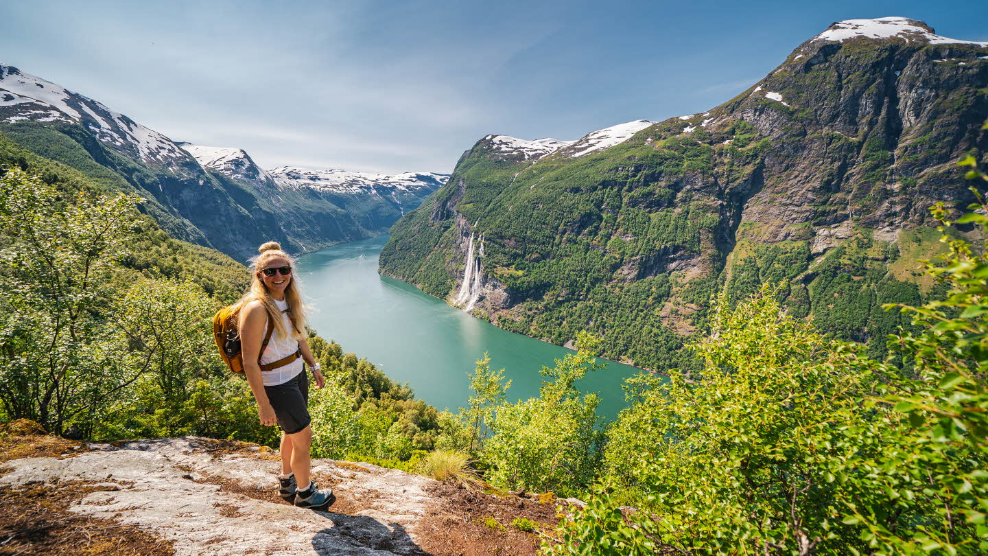 A woman is turning to the camera smiling on a hike above the Geirangerfjord