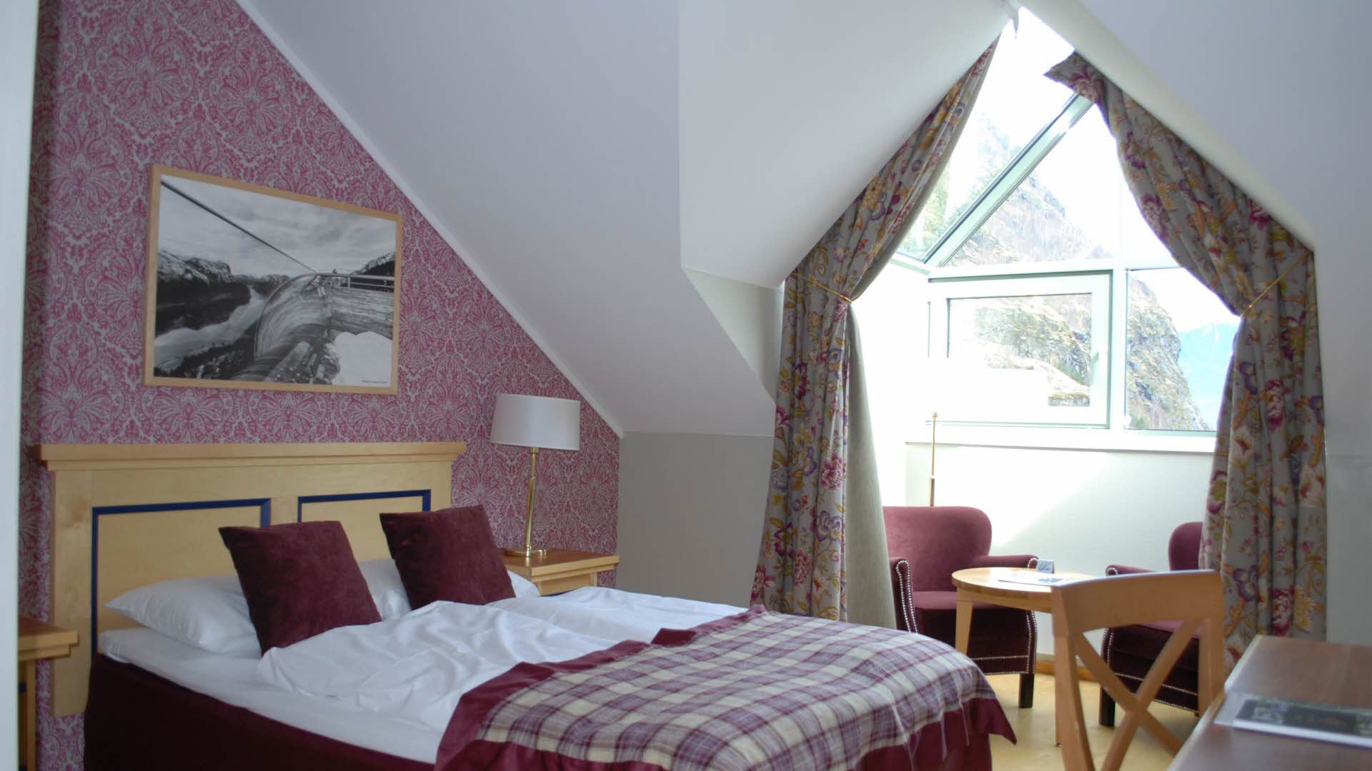 Single room at Fretheim Hotel made up for two people, with queen size bed in front and seating area in bay window in the back. 