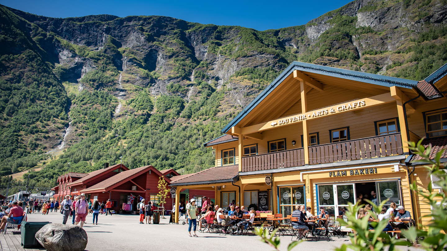 Flåm town centre on a sunny summer day. Tourists walking and sitting outside Flåm Bakery. 