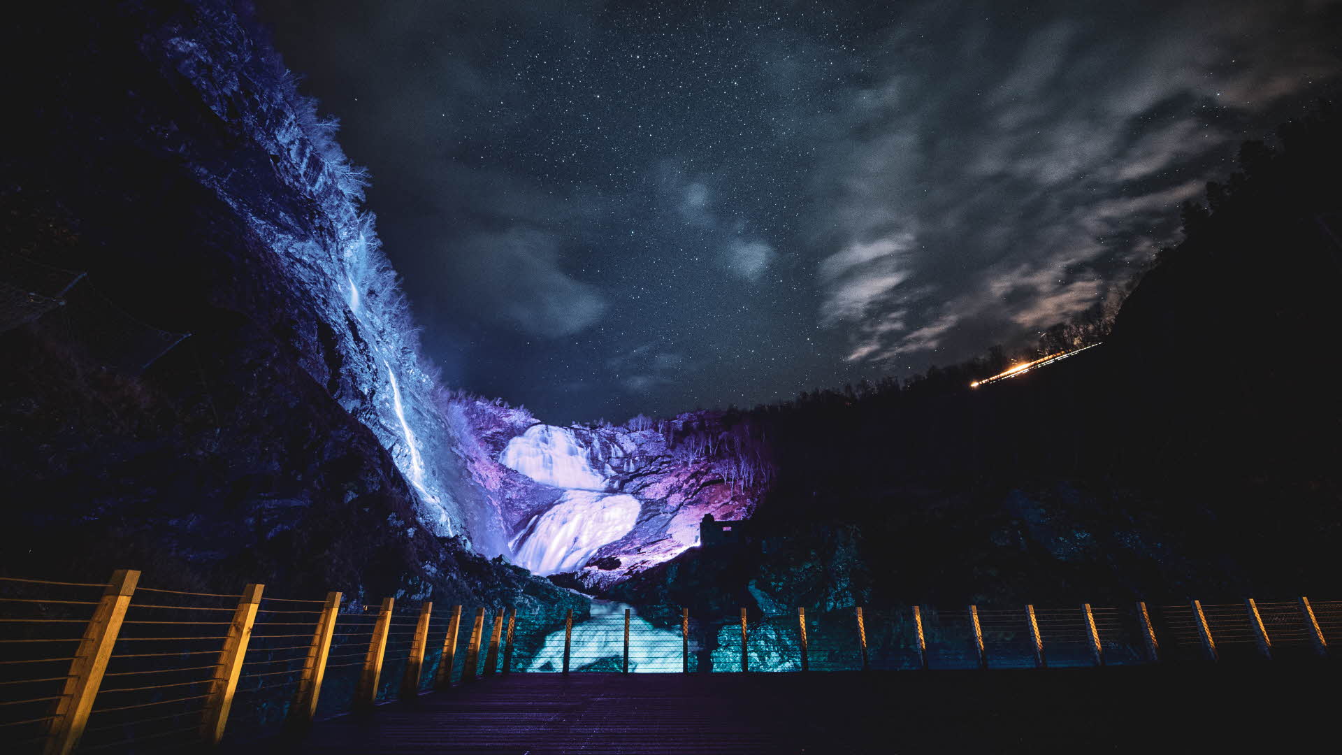 Kjosfossen waterfall illuminated by purple light in the dark.