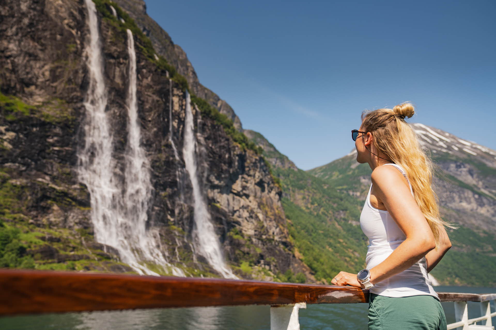 Une femme vue de côté regarde une cascade du Geirangerfjord en se tenant à la balustrade d’un bateau