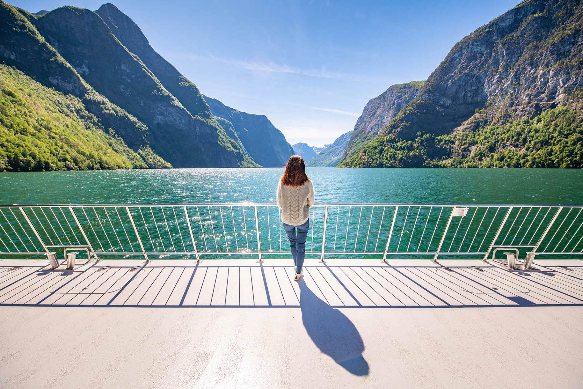 Panoramavisning av kvinne som står foran og midt i Future of The Fjords som seiler gjennom Nærøyfjorden om sommeren