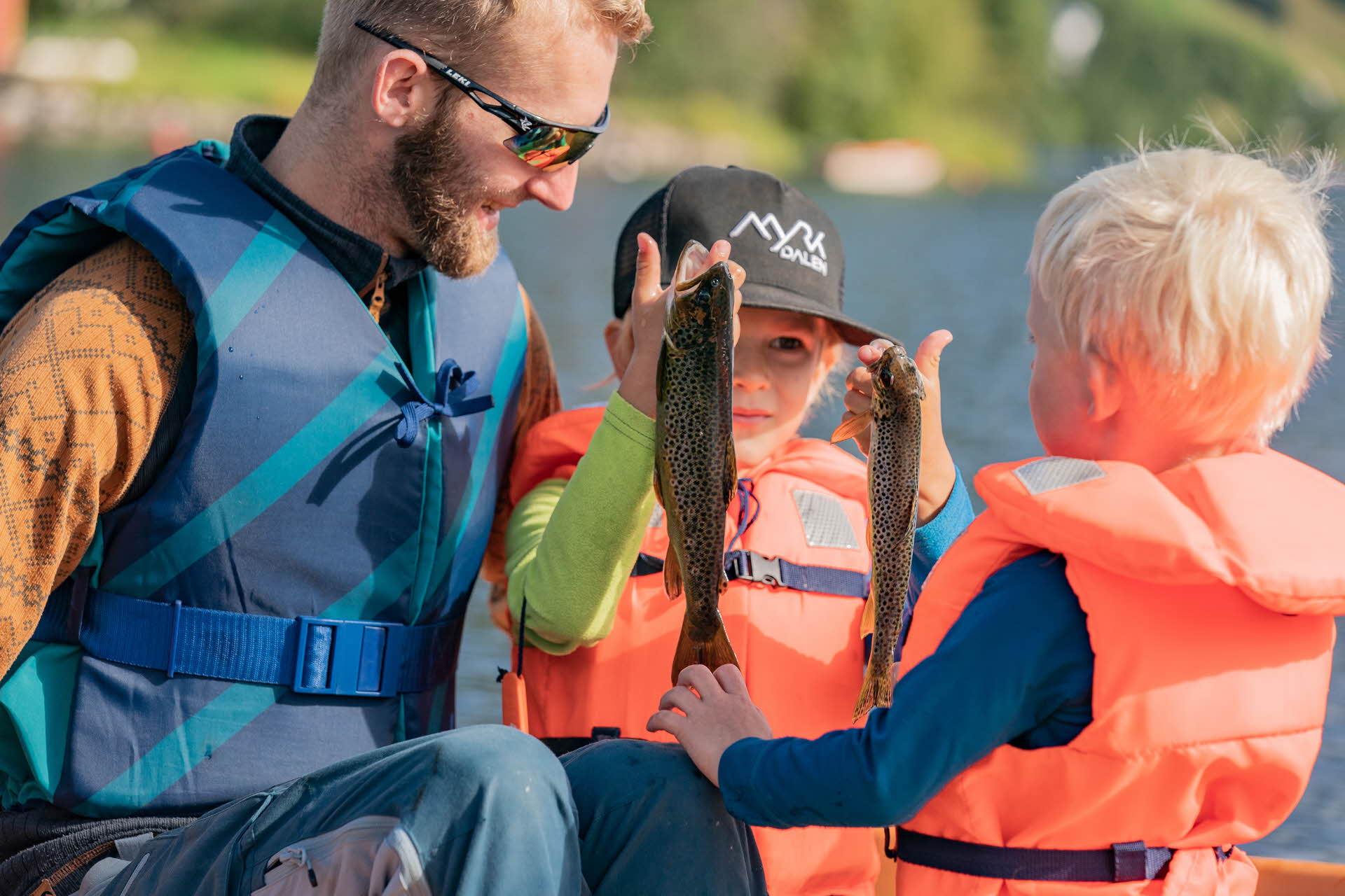 Un hombre y dos niños pequeños con chalecos salvavidas sosteniendo dos peces recién pescados