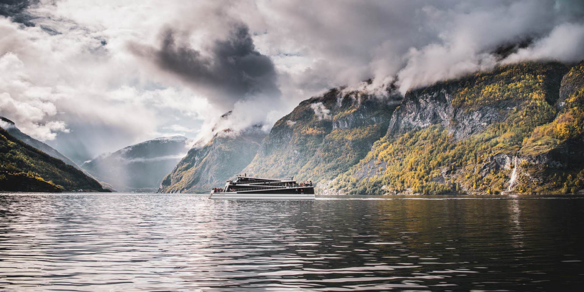 Vue d’ensemble du bateau Future of the Fjords naviguant en automne sur le célèbre Nærøyfjord, inscrit à l’UNESCO, dans une atmosphère calme et nuageuse
