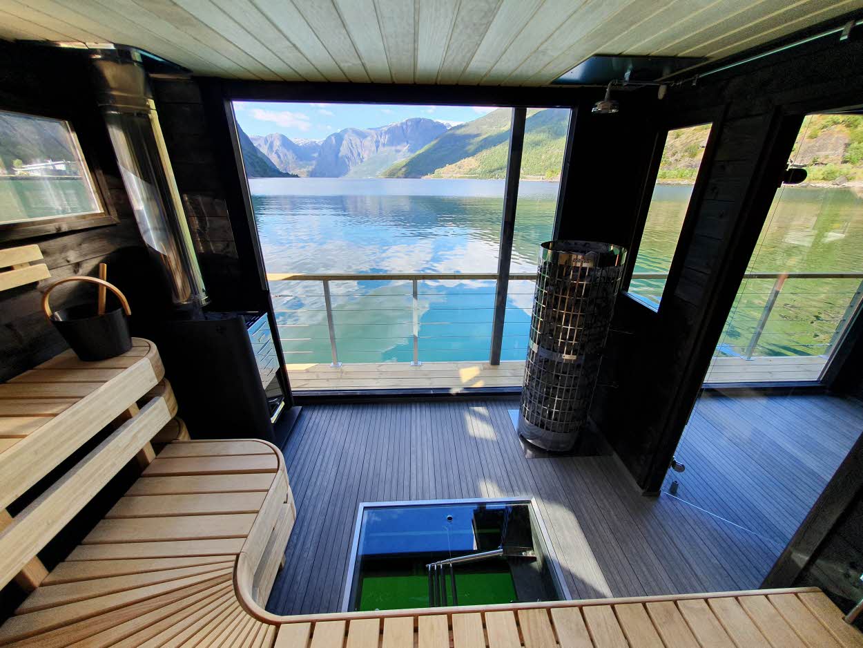 Interior de una sauna flotante en el Aurlandsfjord. Unos bancos de madera, unas calderas, una terraza y unas escaleras que se adentran en el fiordo.