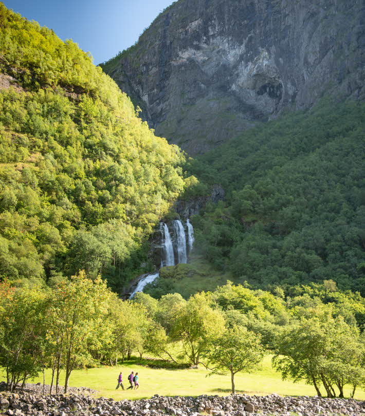 A group of hikers walking on an old path by a waterfall in the Nærøyfjord