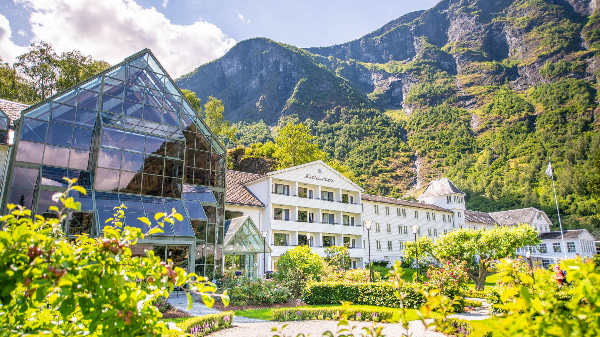 El Hotel Fretheim frente a unas montañas escarpadas vistas desde el jardín en primer plano.
