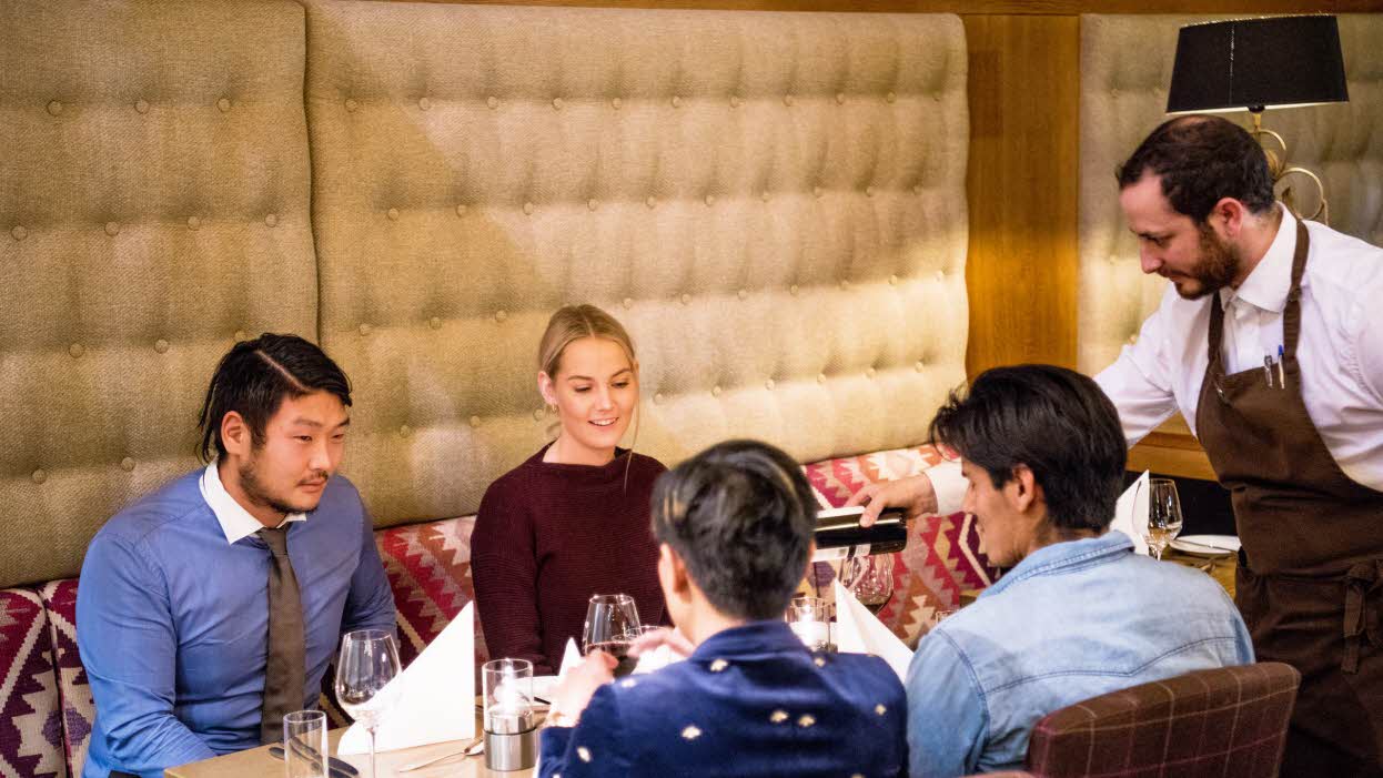 Deux couples attablés au restaurant Arven, avec un serveur versant du vin rouge dans leurs verres