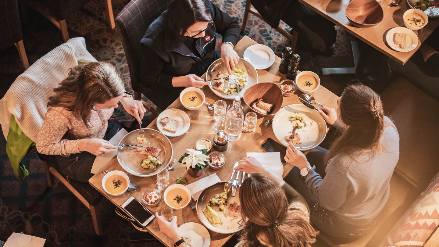 Fire personer sett spisende i restaurant Arven ovenfra. Bordet er fylt med fat og glass. 