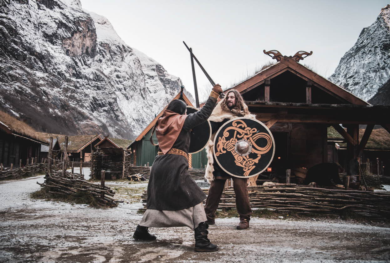 Zwei Personen in Wikingerkleidung kämpfen im winterlichen Wikingertal Gudvangen mit Schwertern und Schilden. Foto.