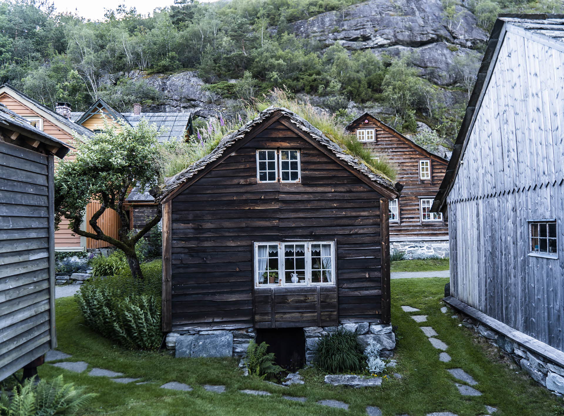Lite brunt trehus Agatunet Hardanger Norge tidlig 1220 gras på tak hviler på natursteiner