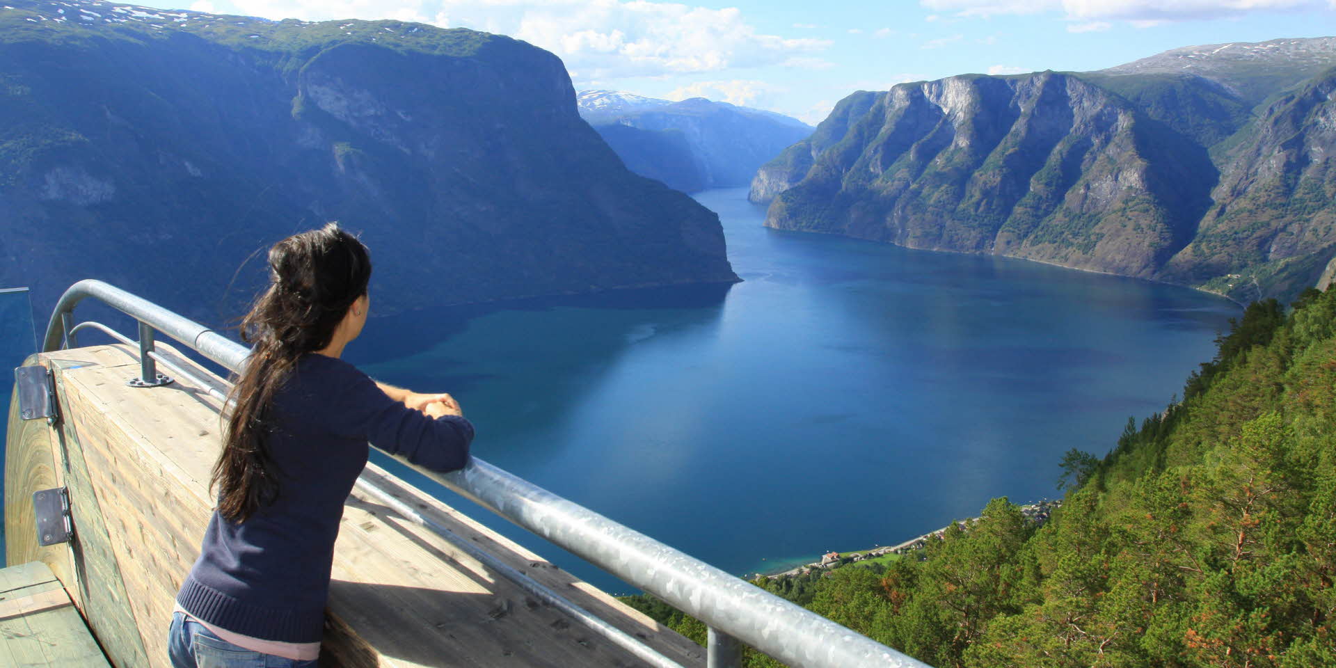 Mujer sobre la plataforma del mirador de Stegastein en verano mirando a Aurlandsfjord