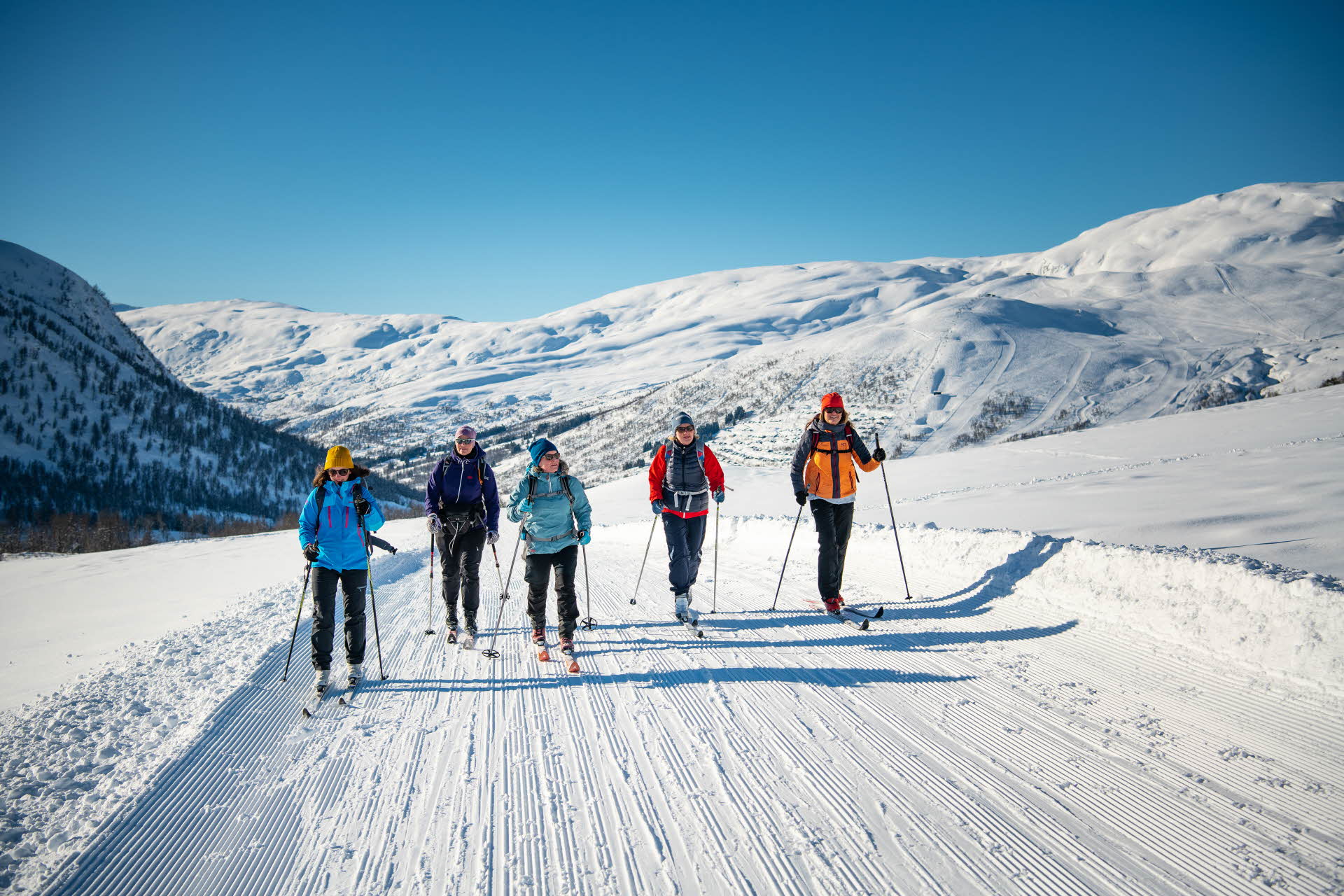 Fem kvinner går på turski i en løype med Myrkdalen Fjellandsby bak.