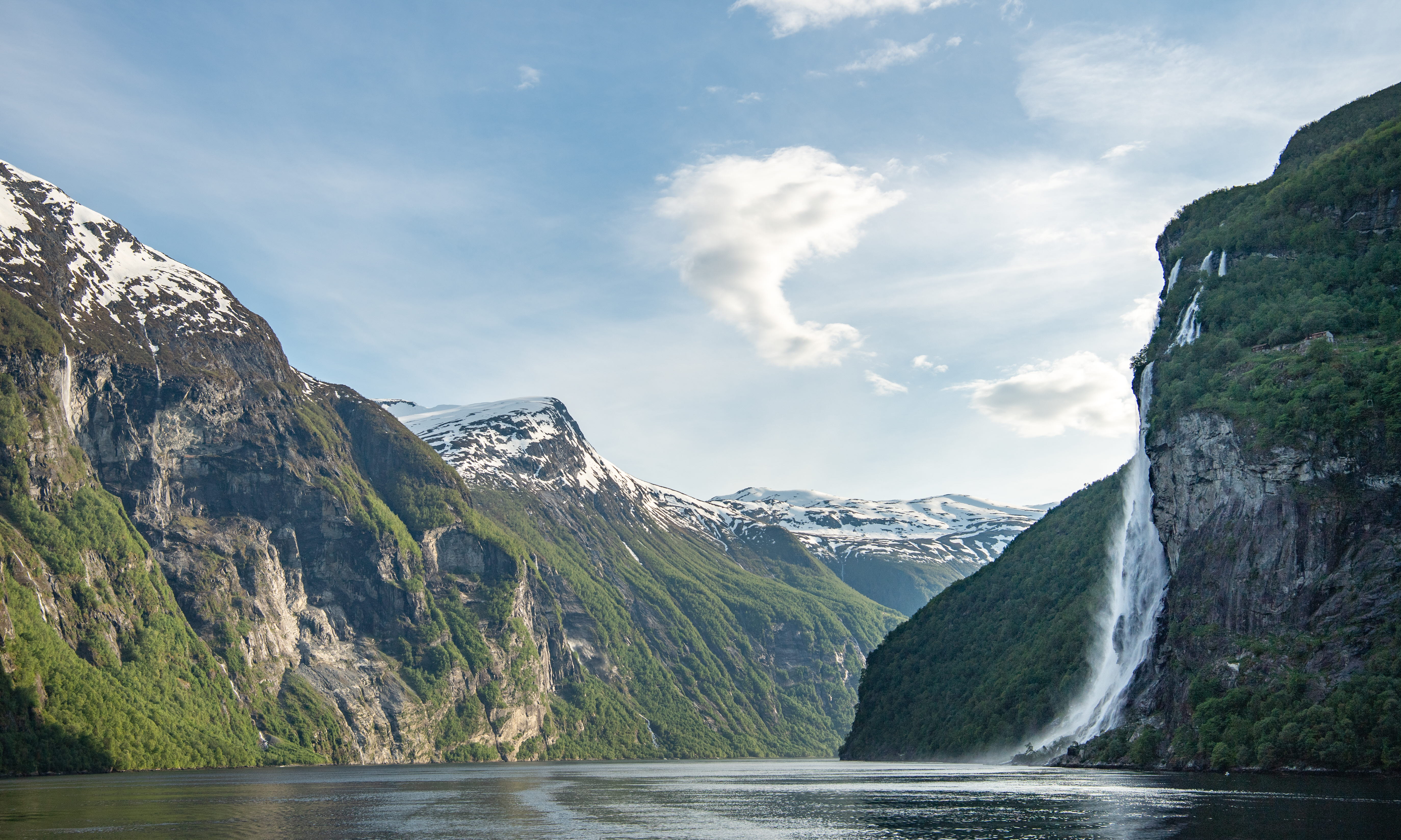 Ein früher Sommertag am Geirangerfjord mit einem großen Wasserfall und schneebedeckten Berggipfeln