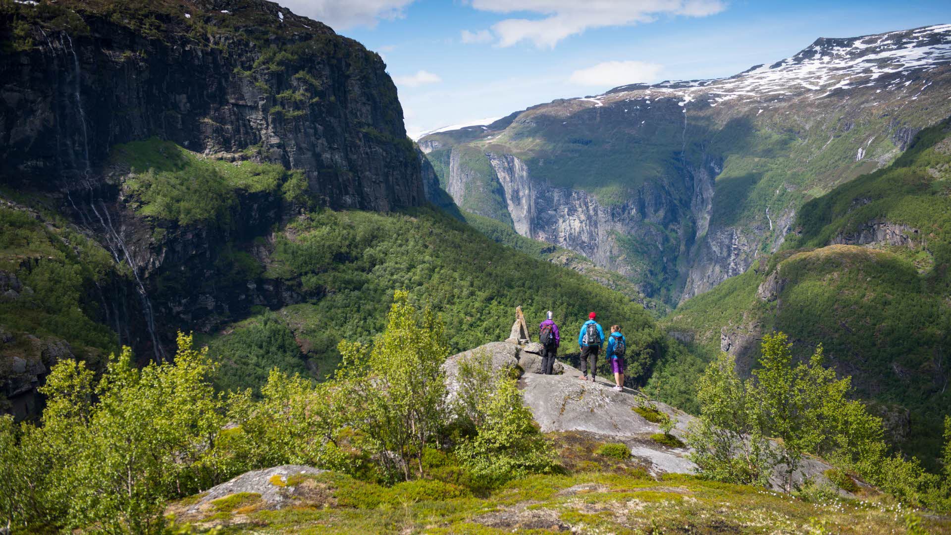 Des randonneurs debout sur un rocher près d’un cairn sont émerveillés par le paysage de la vallée d’Aurland. 