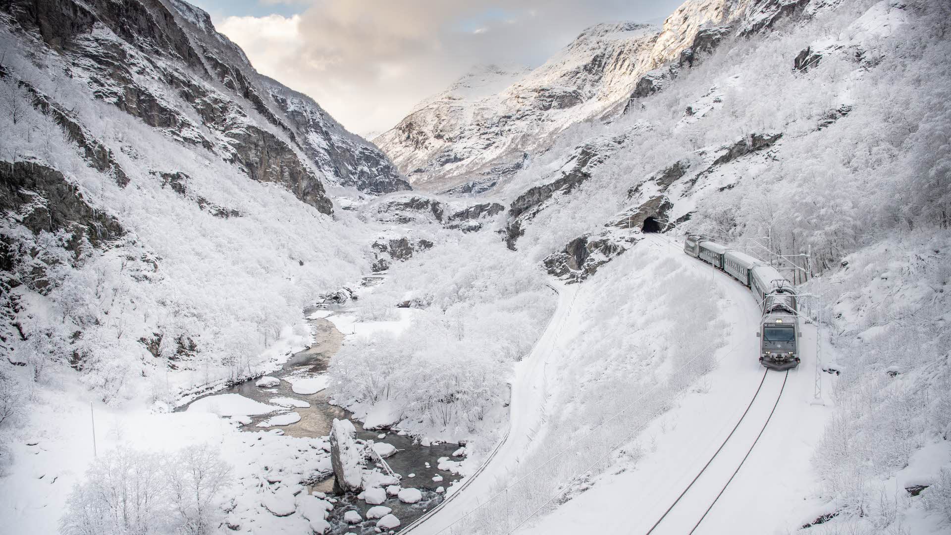 一辆火车行驶在 Flam 山谷里。周围是白雪皑皑的景色。 