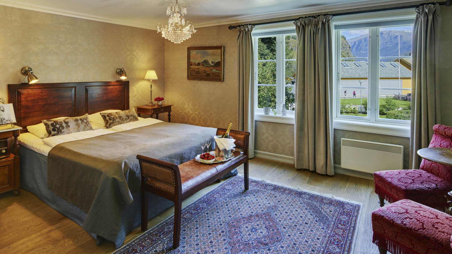 A historic room with vintage furniture, champagne and berries on a bench and windows with views to Flåm