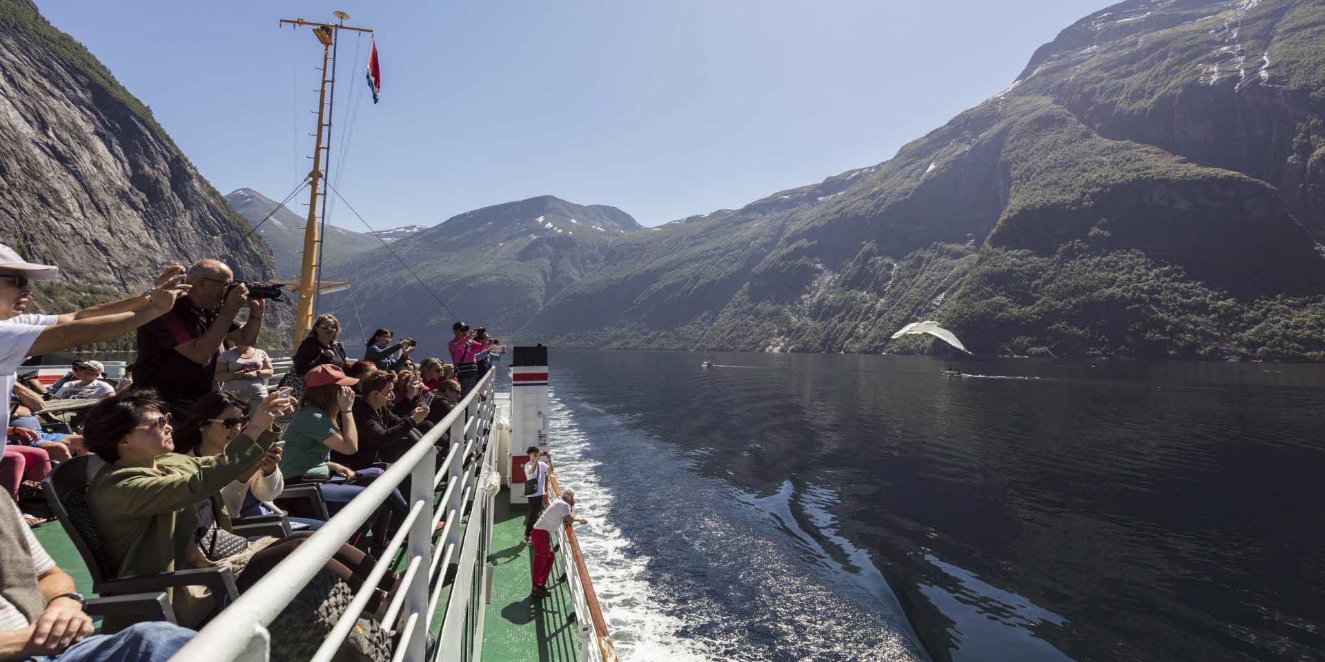 Des gens prenant des photos profitent du fjord et des montagnes en été sur le pont-terrasse d’un bateau de croisière dans le Geirangerfjord