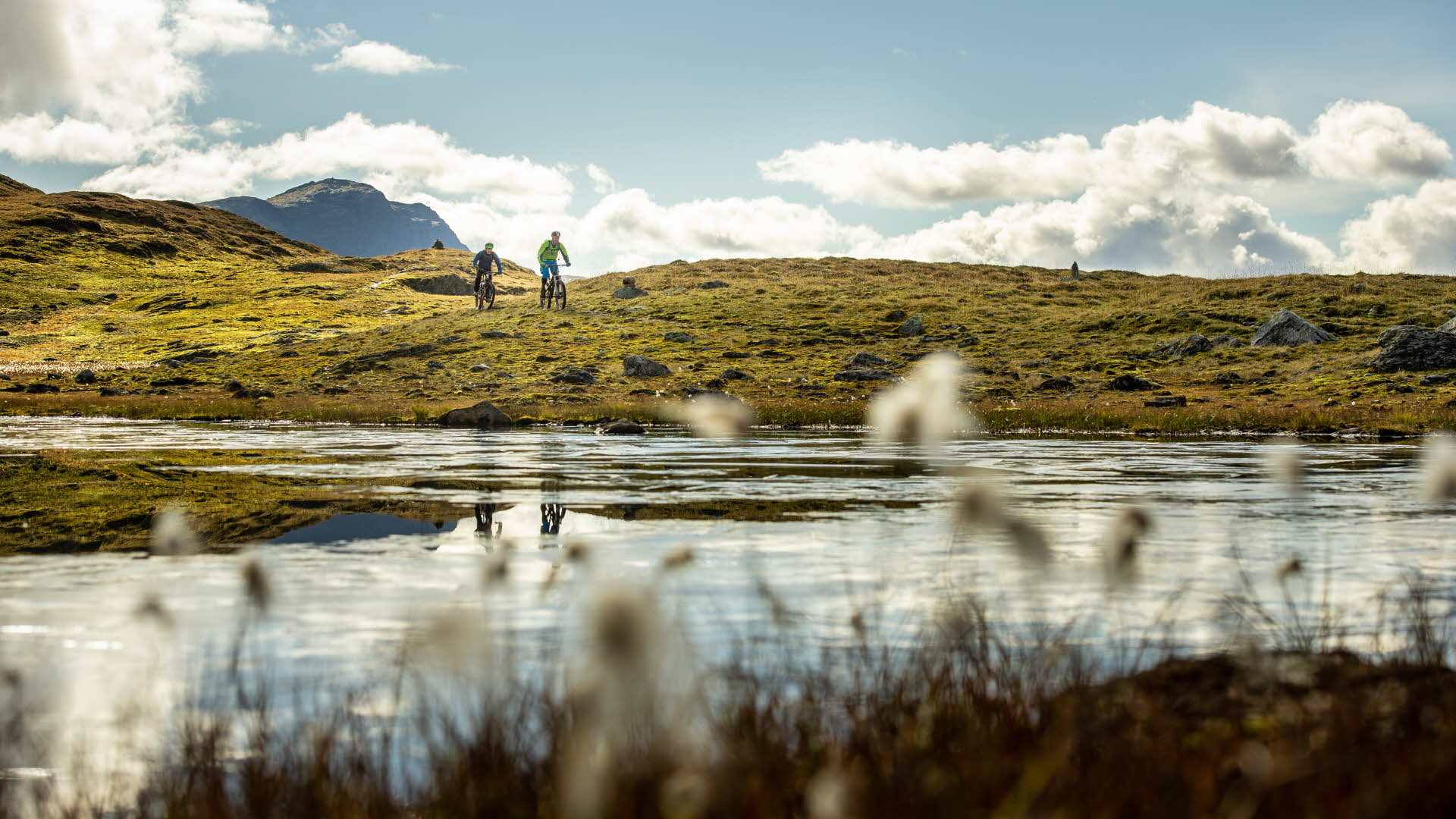 さわやかな夏の日に池のほとりを走る2人のサイクリストと山の地形。 
