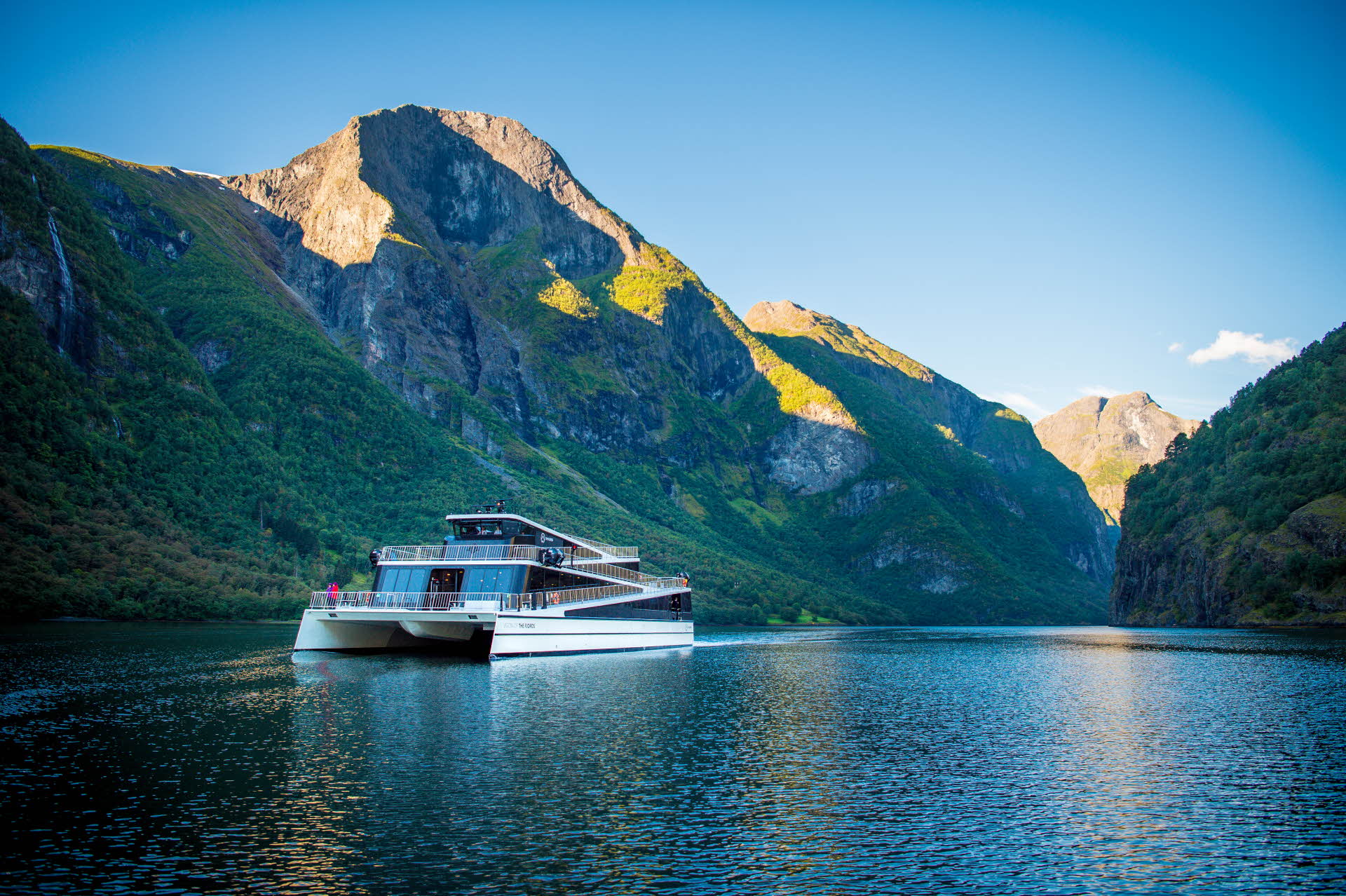Die „Future of The Fjords“ fährt im Sommer auf dem ruhigen und engen, zum UNESCO-Welterbe gehörenden Nærøyfjord, im Hintergrund sind hohe Berge zu sehen.
