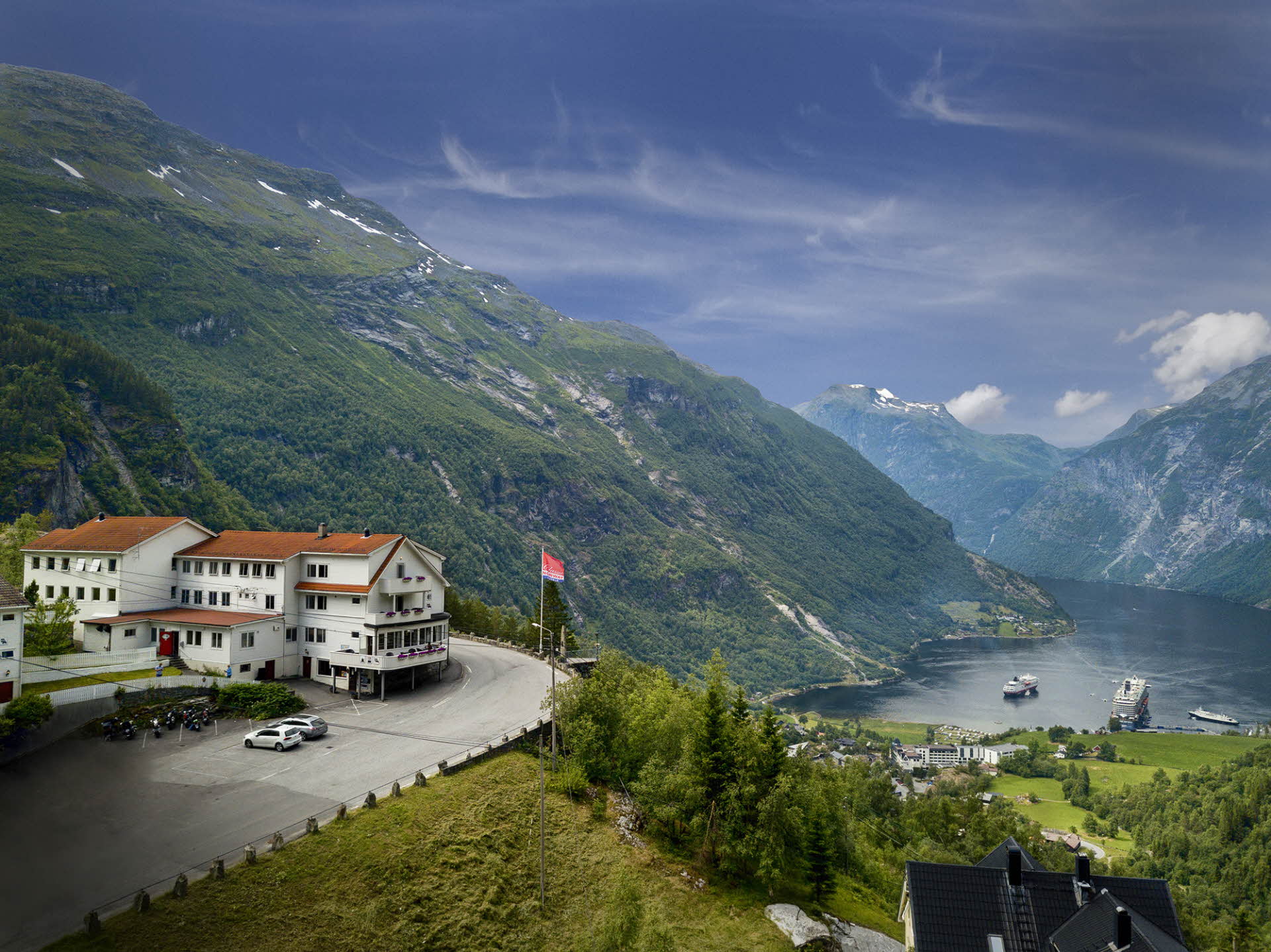 View of Hotel Utsikten above Geiranger and the fjord. Mountains, blue sky and green forest.