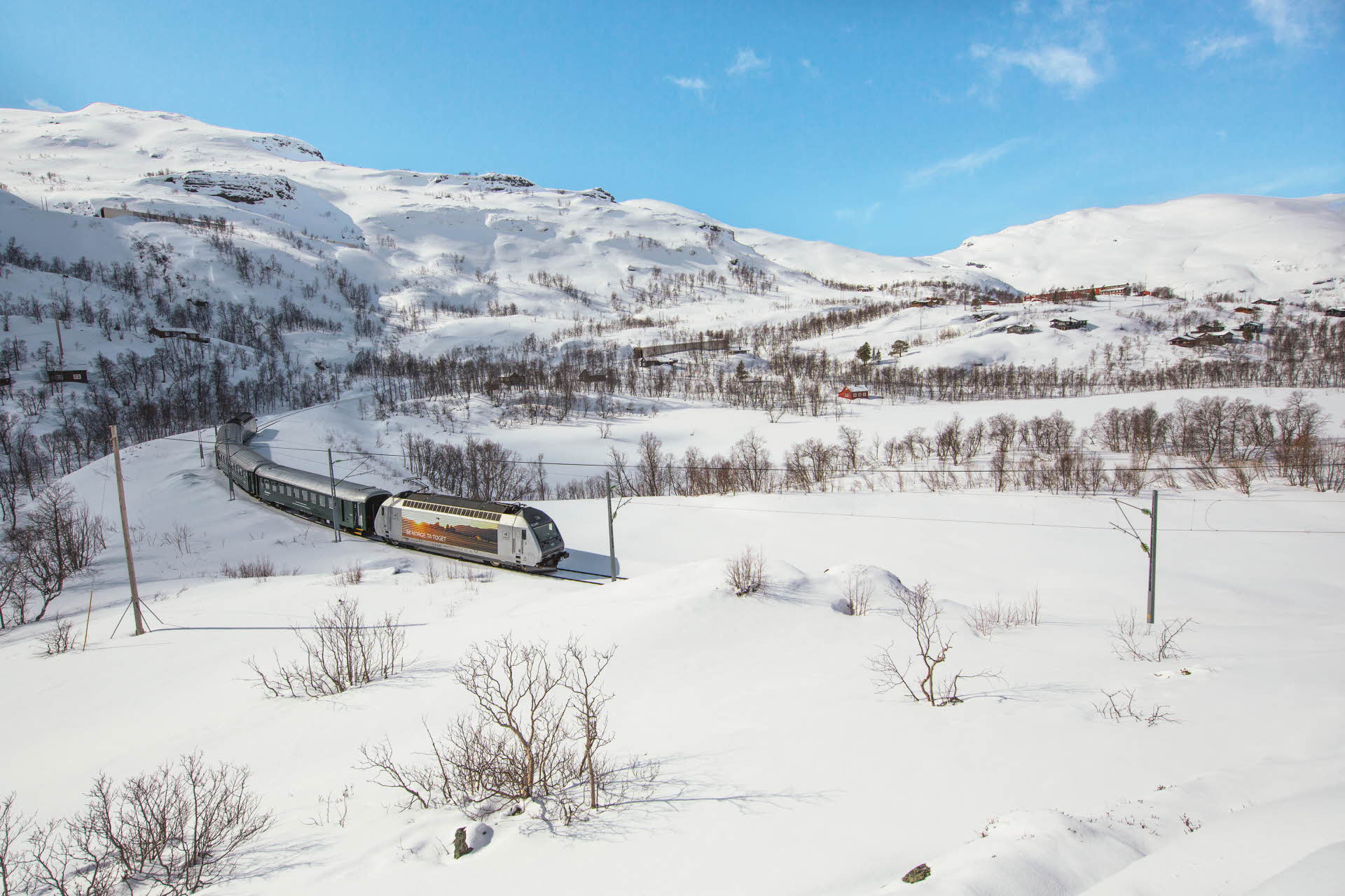 Le train de Flåm traverse un paysage montagneux et enneigé par une belle journée d’hiver. 
