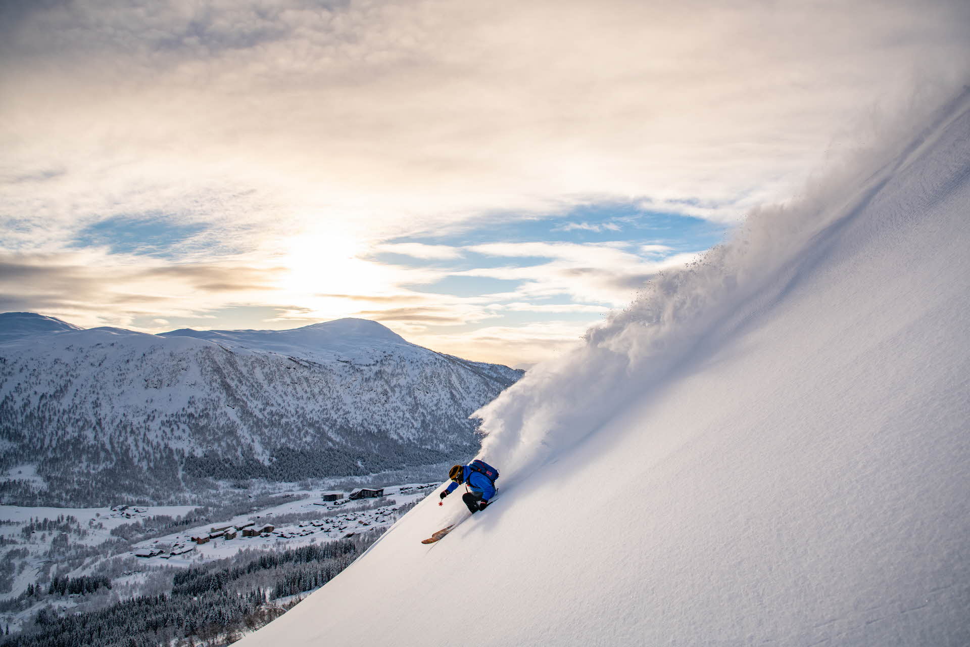在一个阳光明媚的日子里，一名穿着蓝色夹克的人在新鲜的粉雪上滑雪。