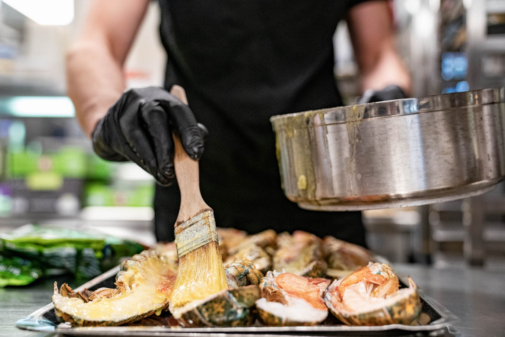 A chef in a black apron marinating lobster with a brush.