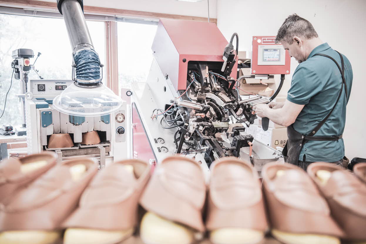Un cordonnier debout devant une machine et trois paires de chaussures Aurland en cours de fabrication au premier plan