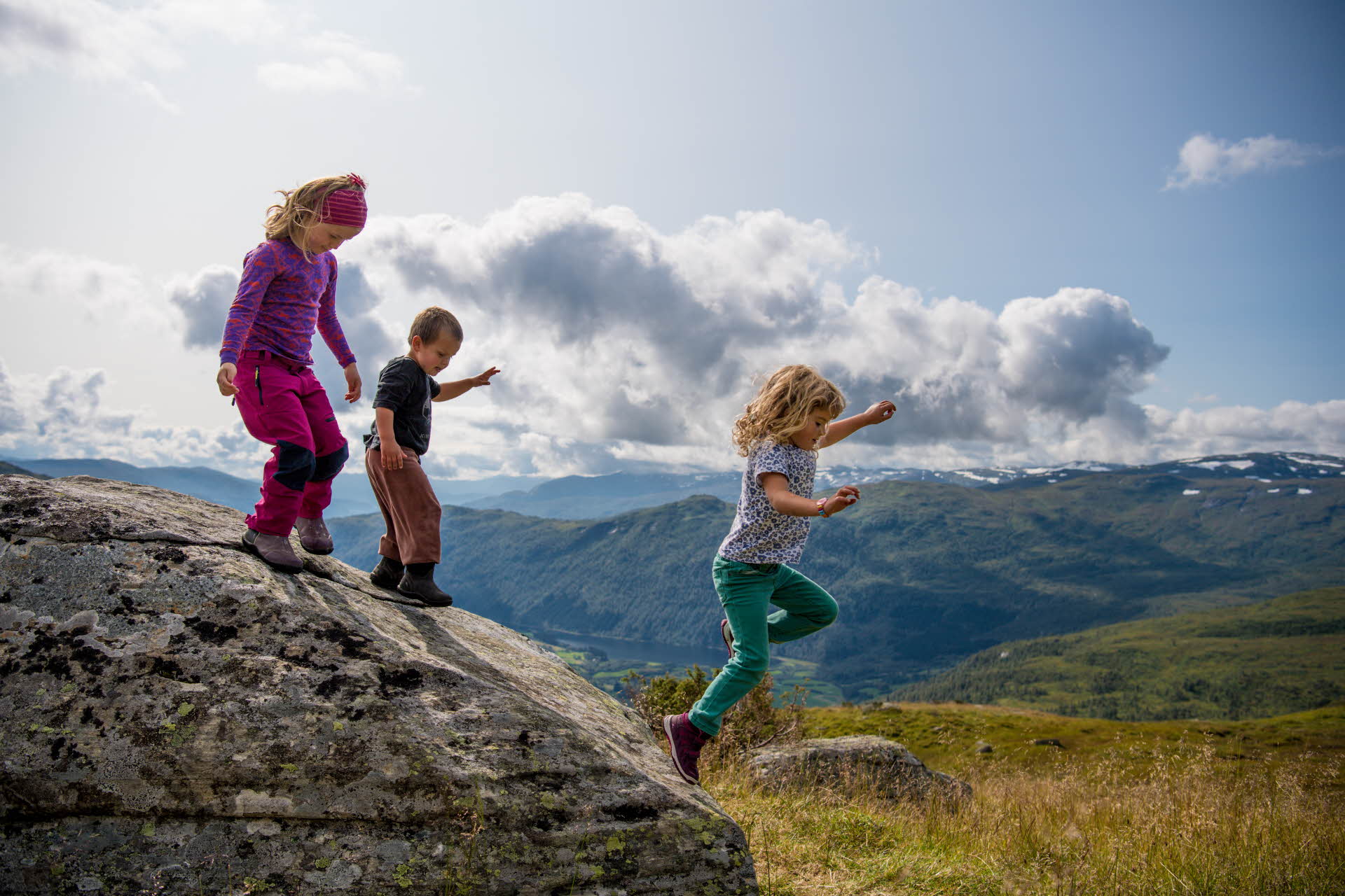 Zwei Mädchen und ein Junge springen bei einer Bergwanderung im Myrkdalen von einem Felsen