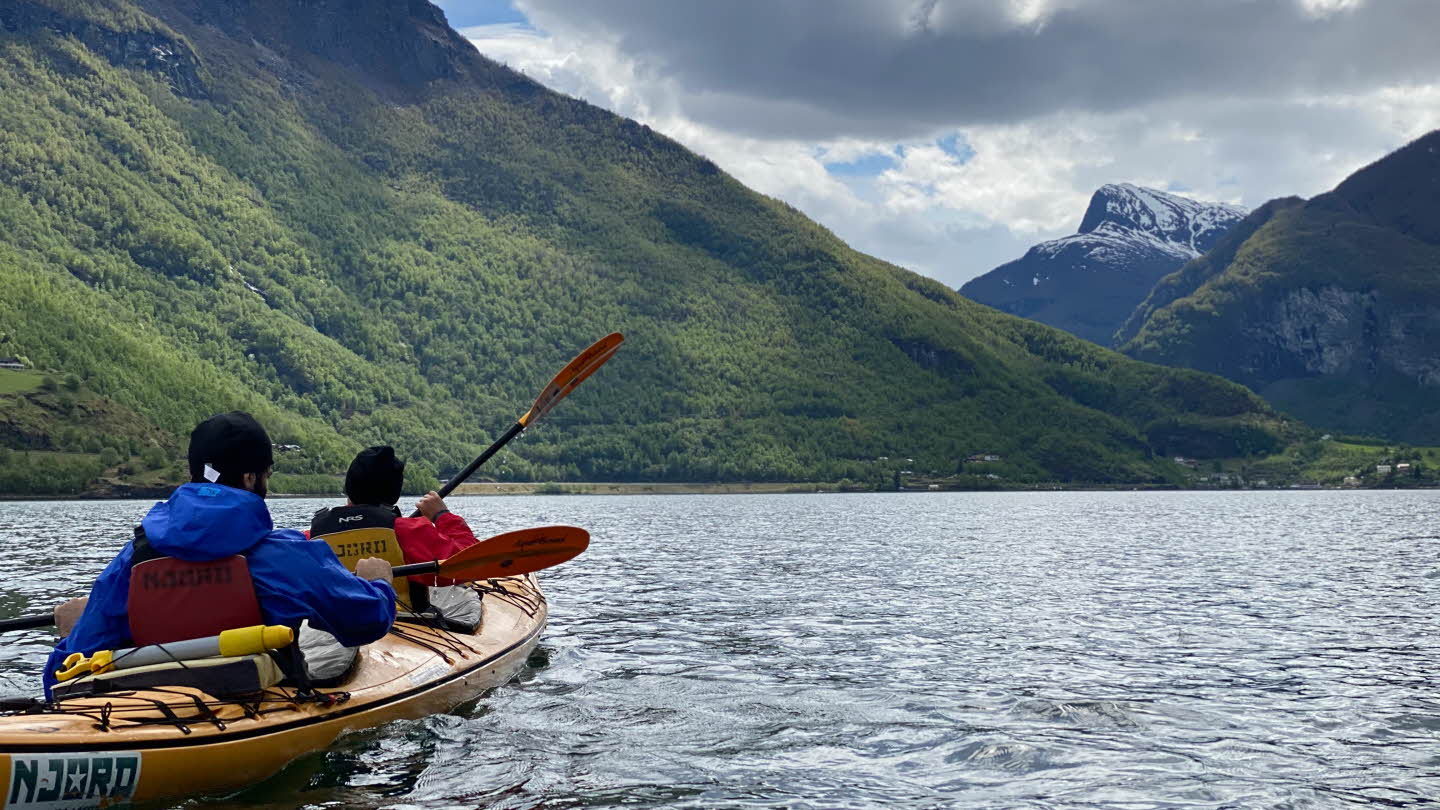 Two people in a tandem kayak on the Aurlandsfjord paddling towards Flåm. Cloudy weather.