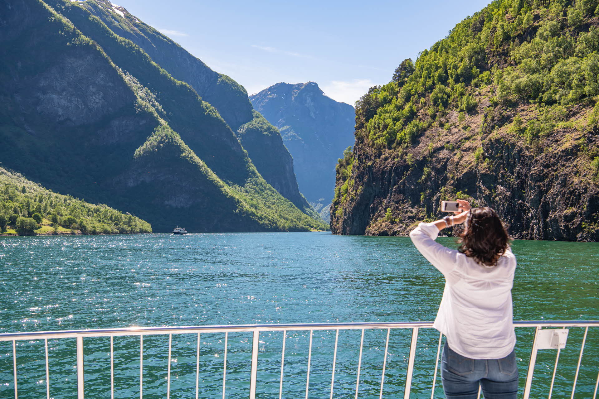 A lady taking a photo of the Nærøyfjord from the bow of the Future of the Fjords