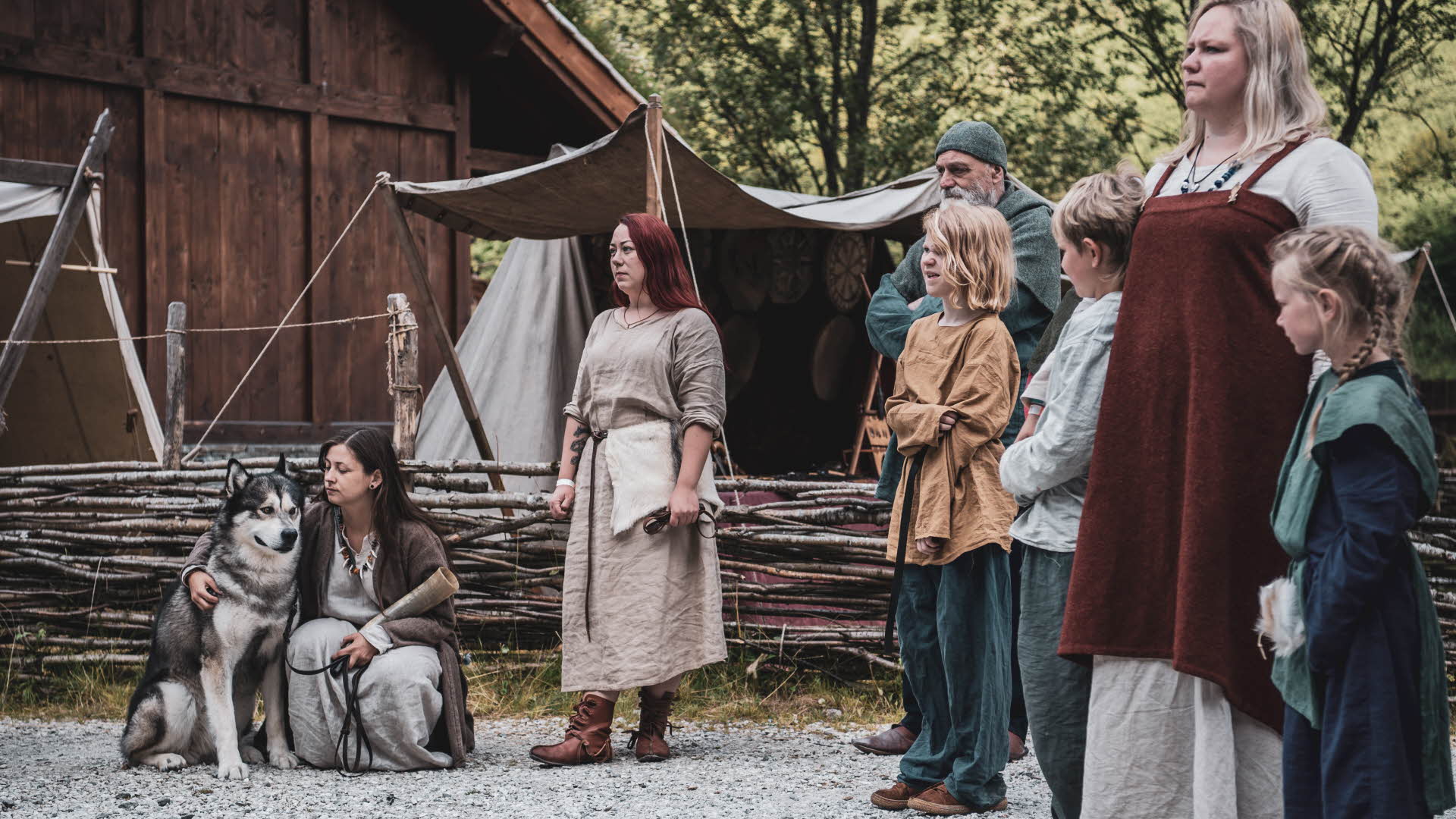 Le village viking à Gudvangen, une famille viking et un husky se tenant à l’extérieur d’un bâtiment authentique en habits traditionnels vikings