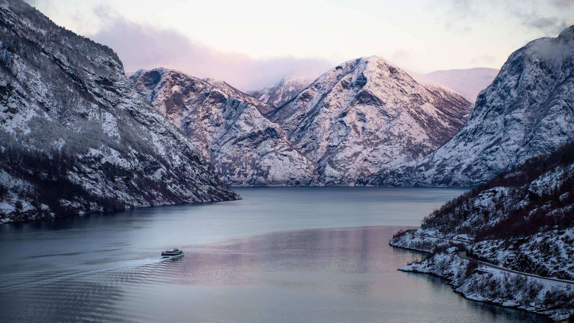 Ein Boot fährt auf dem Aurlandsfjord. Gedämpftes Licht und schneebedeckte Berge.