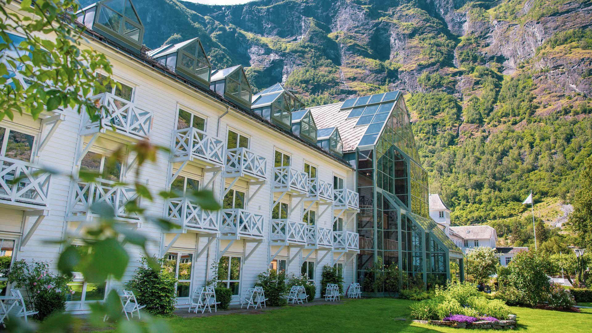 Fretheim Hotel sett fra hagen med grønne blader i front og bratte fjellsider bak. 
