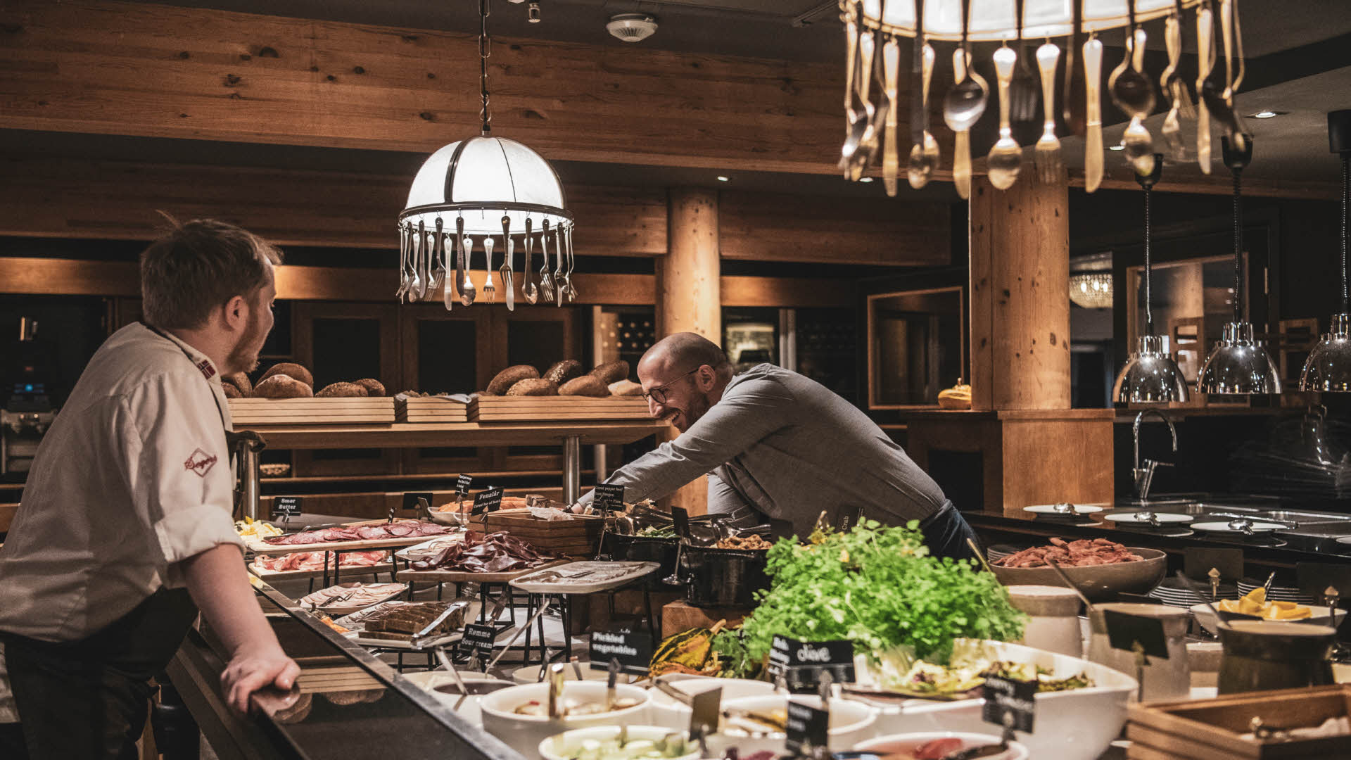 Un chef y un camarero ultiman los detalles del buffet del Hotel Fretheim. Unas lámparas con detalles de cubiertos.