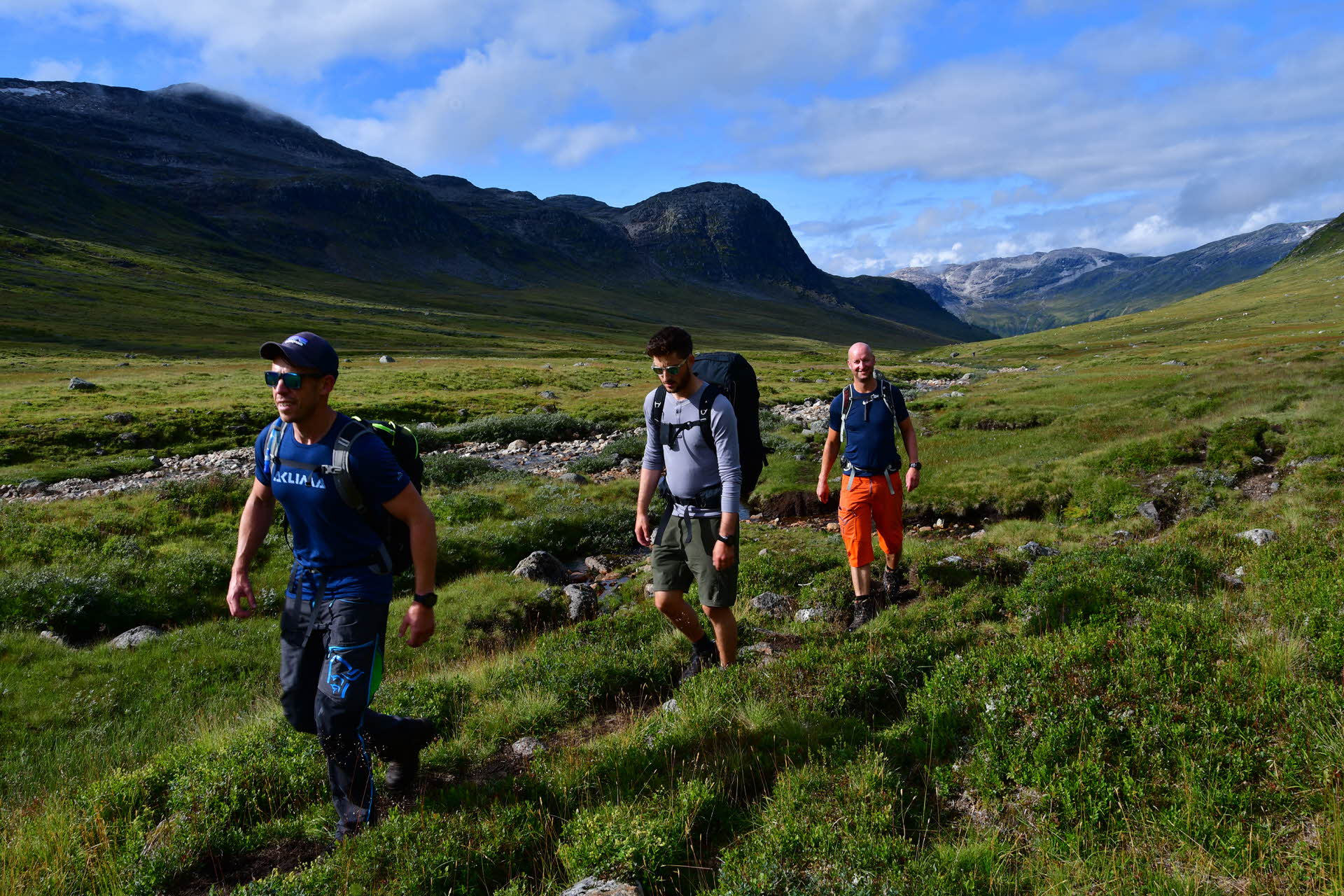 Trois hommes marchent le long d’un sentier dans une vallée verdoyante et vallonnée
