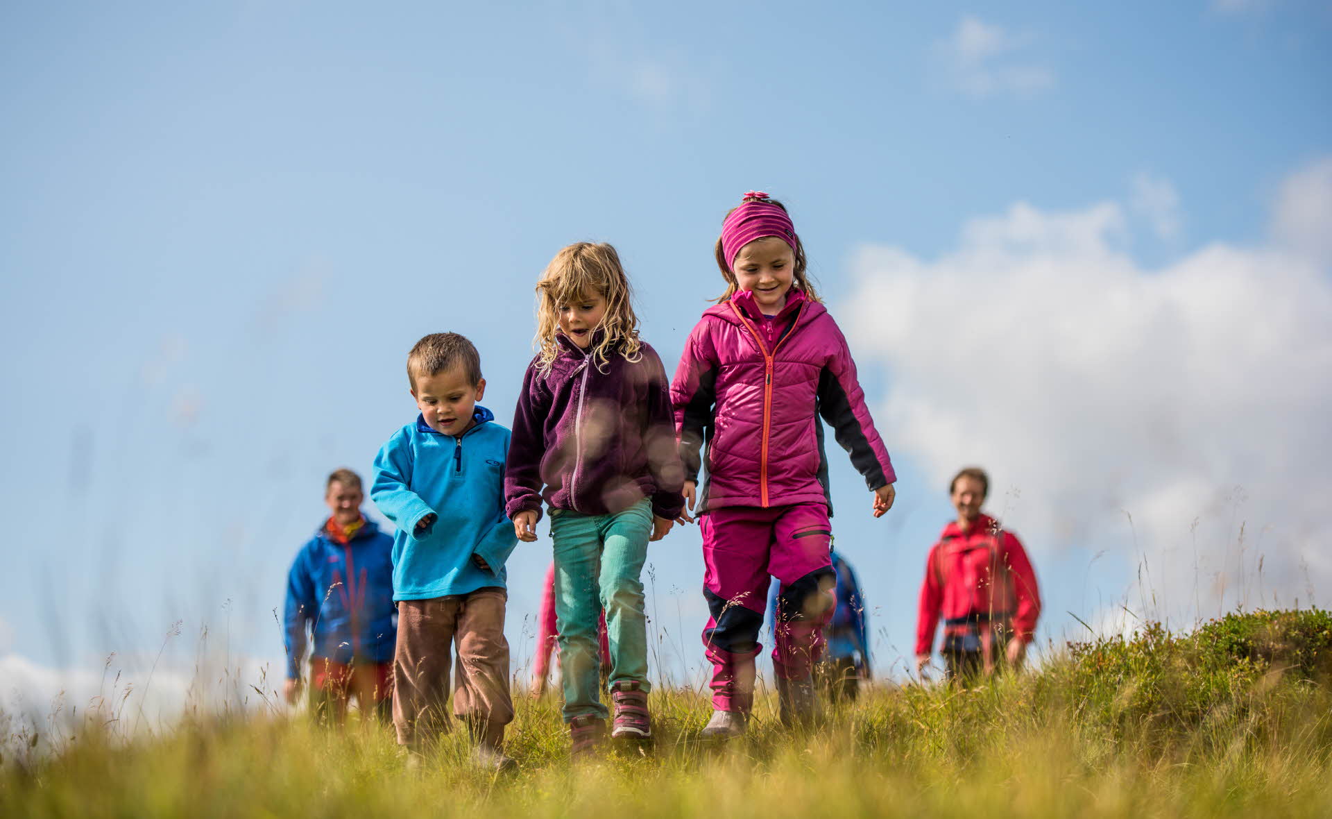 Drei lächelnde Kinder auf einer Wanderung in Myrkdalen, mit vier Erwachsenen dahinter